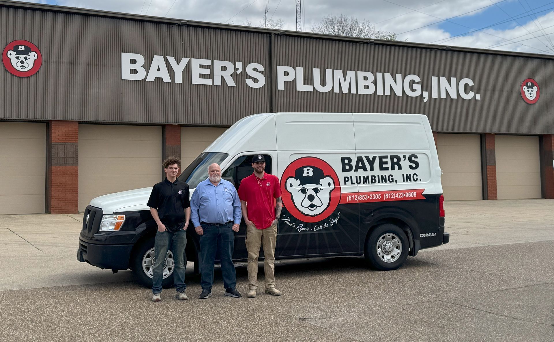 Bayer’s Plumbing van parked outside storefront, with four people standing in front of it.