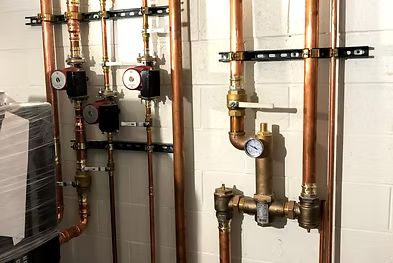 Indoor boiler room with copper pipes, valves, and pressure gauges mounted on a white wall