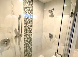 Modern white bathroom with glass shower, chrome fixtures, and a decorative mosaic tile strip