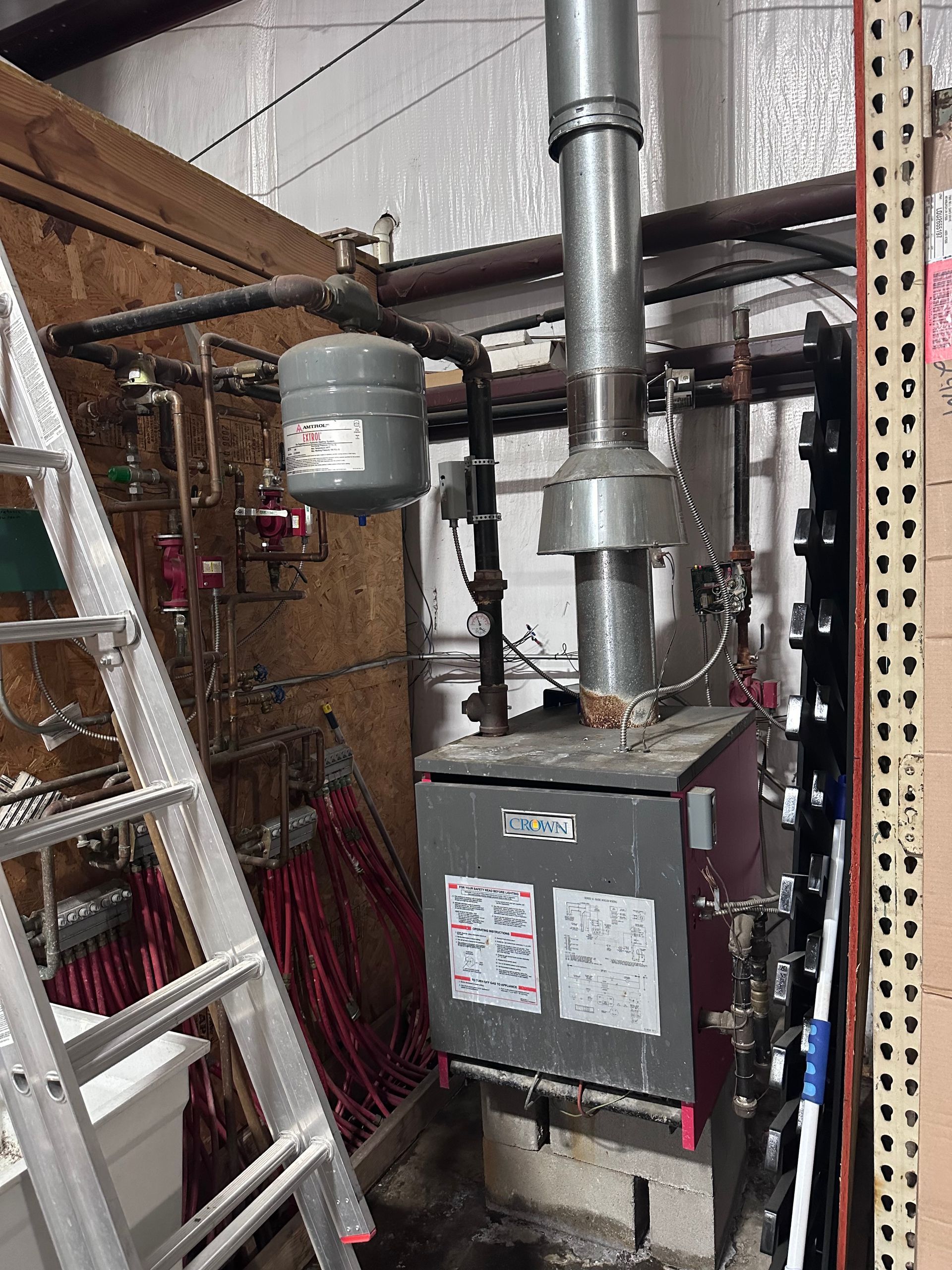 Boiler room with metal furnace, chimney pipes, ladder, and bundled red cables in a cluttered utility space