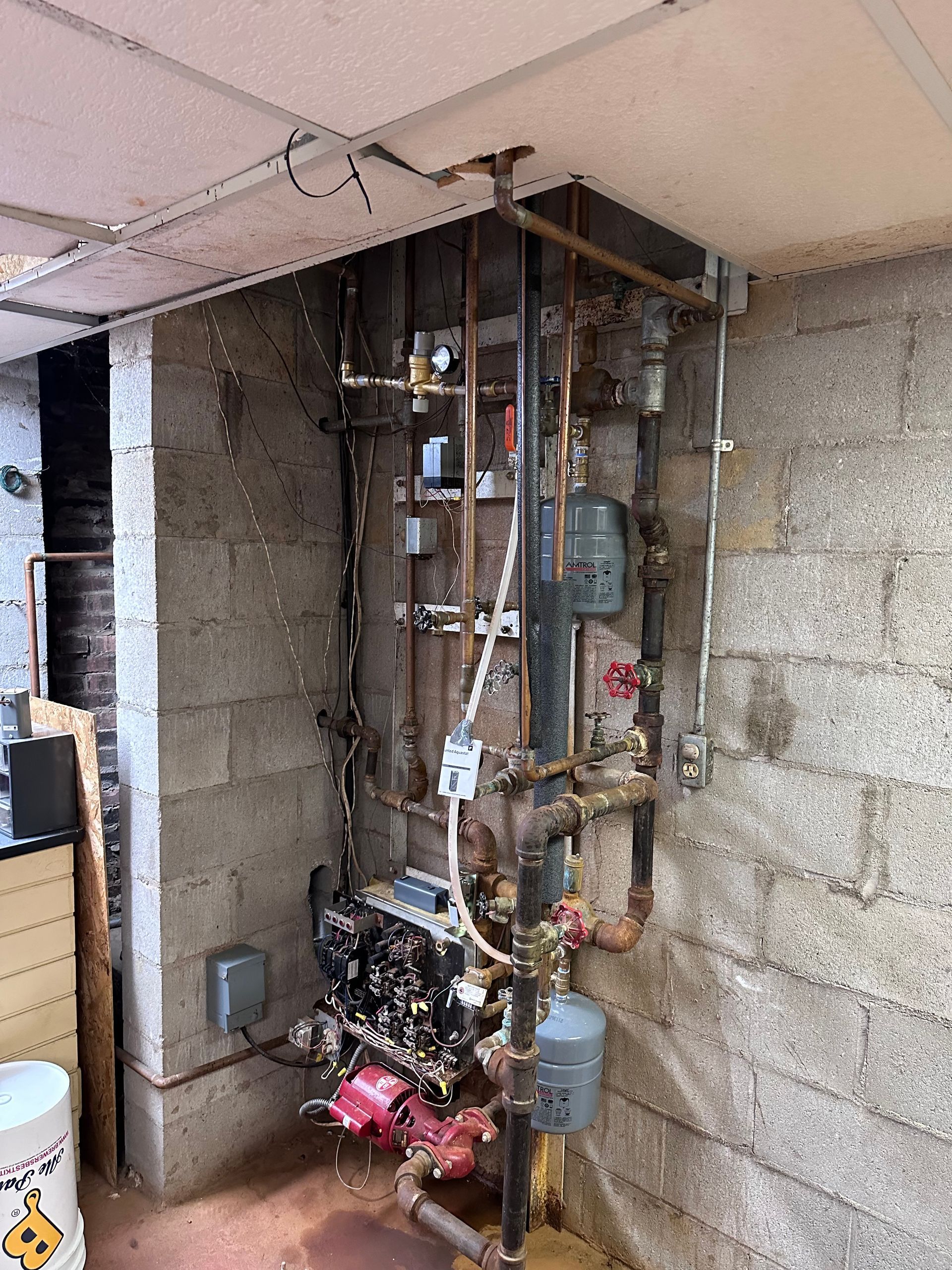 Exposed water heater and plumbing inside unfinished basement wall, with pipes, wires, and concrete blocks