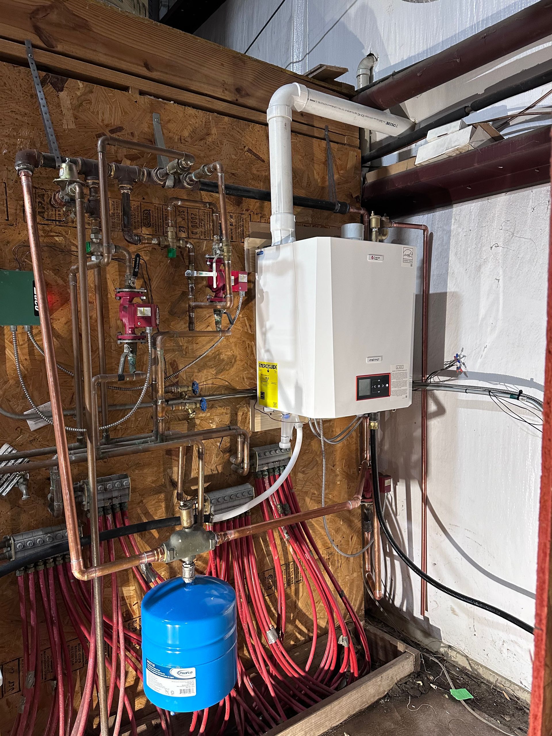 Electrical panel with tangled red wiring, a white wall-mounted unit, and a blue tank in a utility room