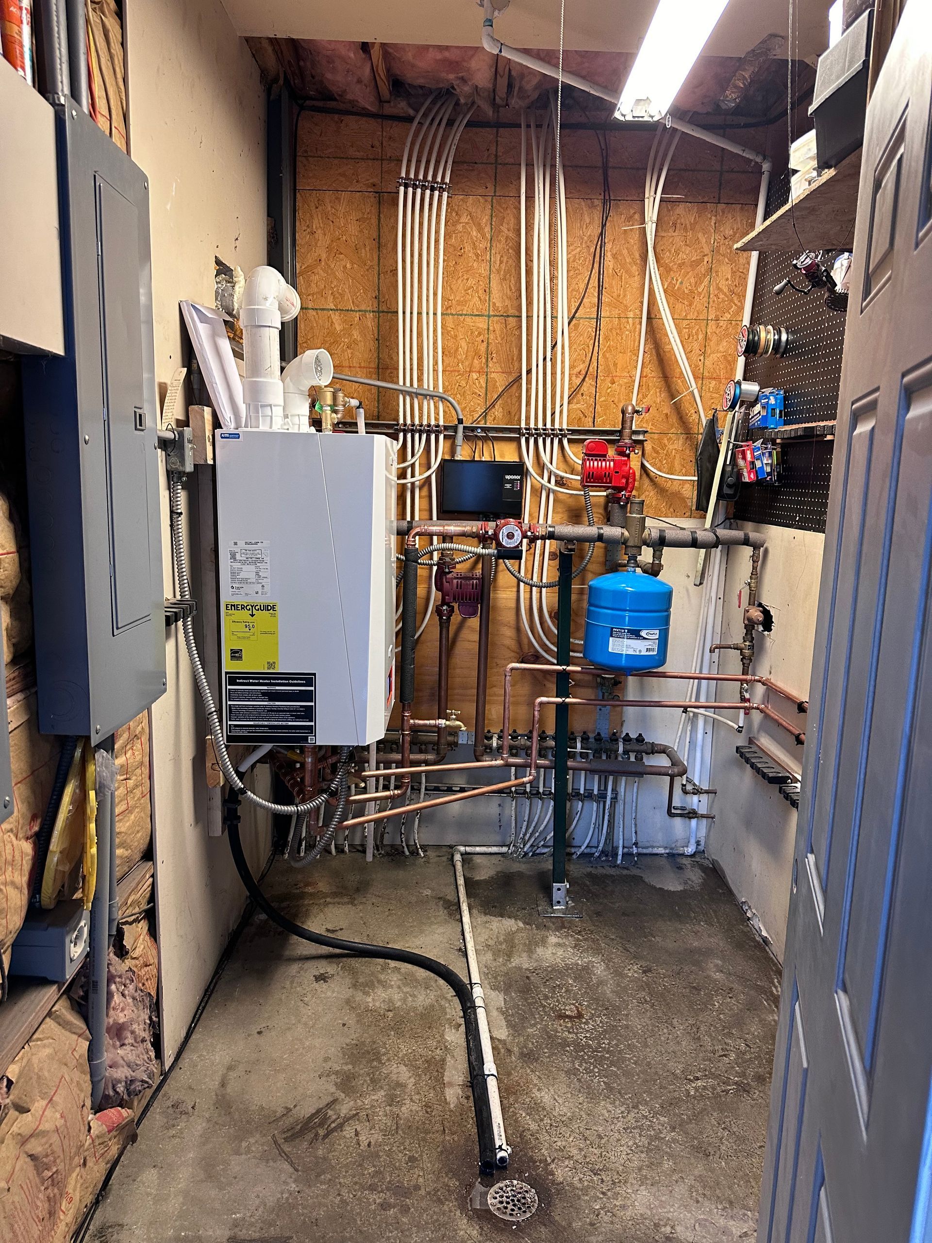 Utility room with boiler, pipes, hoses, and shelving on a concrete floor.