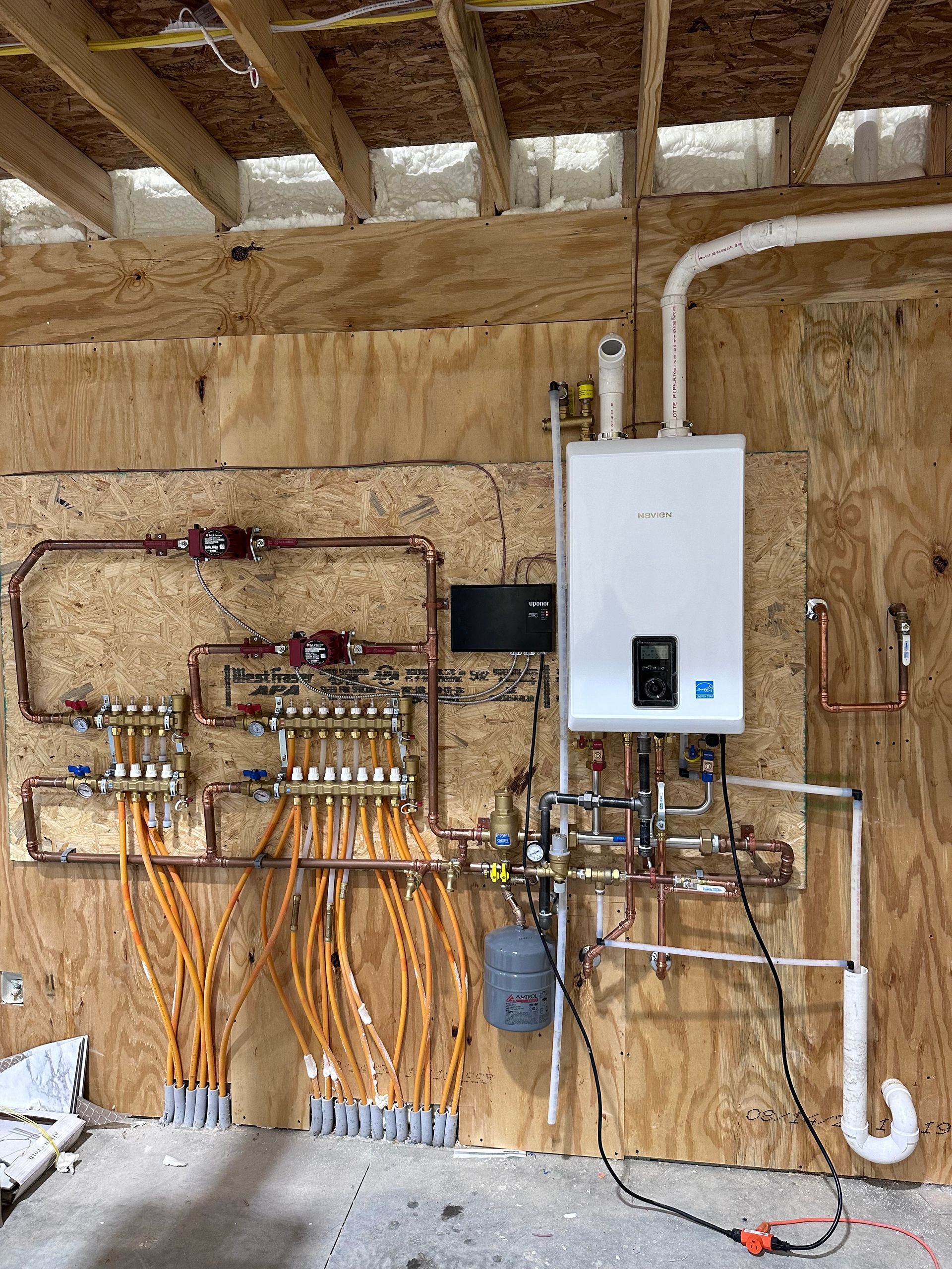 Interior wall with a white water heater and exposed copper piping, valves, and plumbing manifold in a utility room