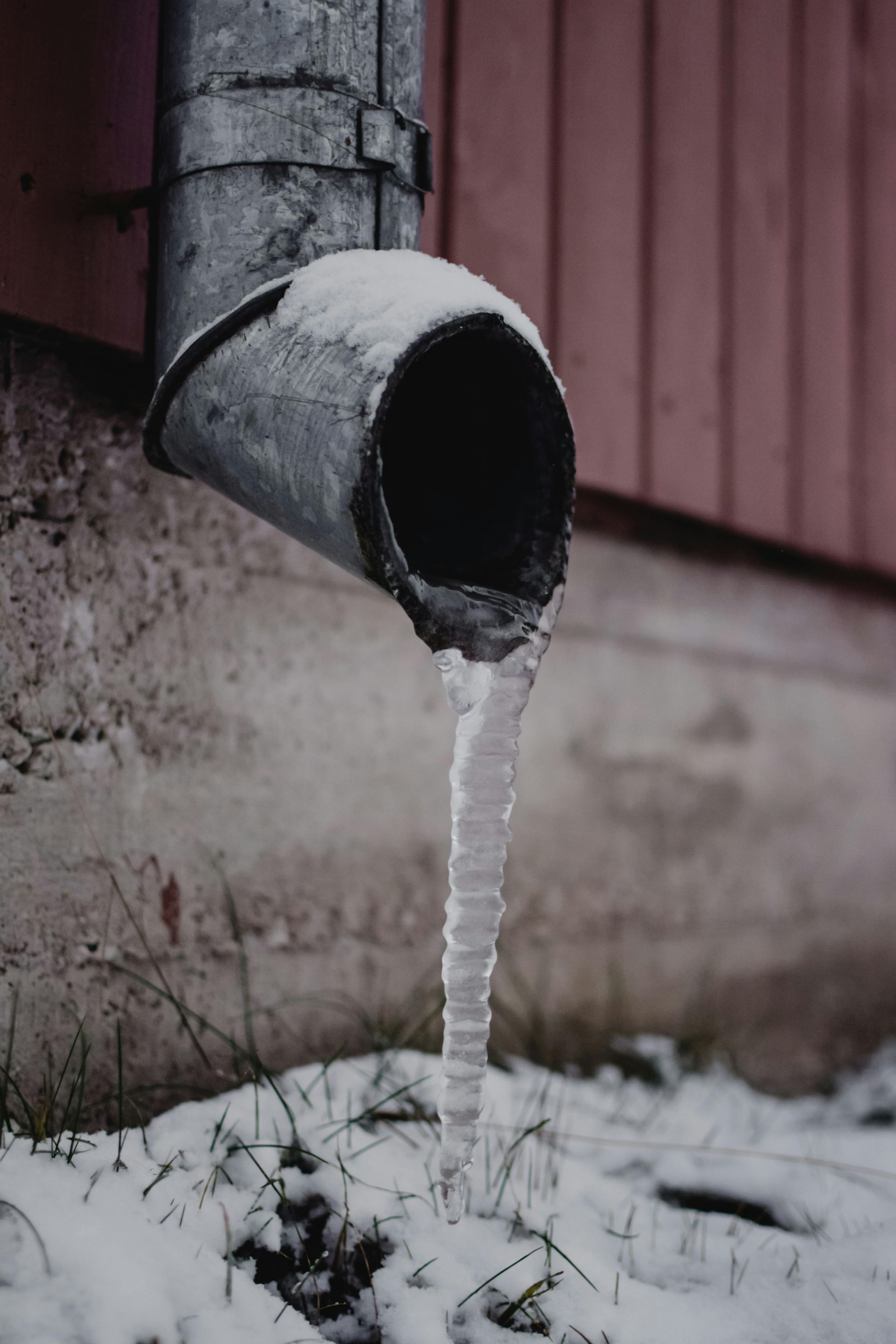 Frozen downspout dripping icicles beside a building wall in winter
