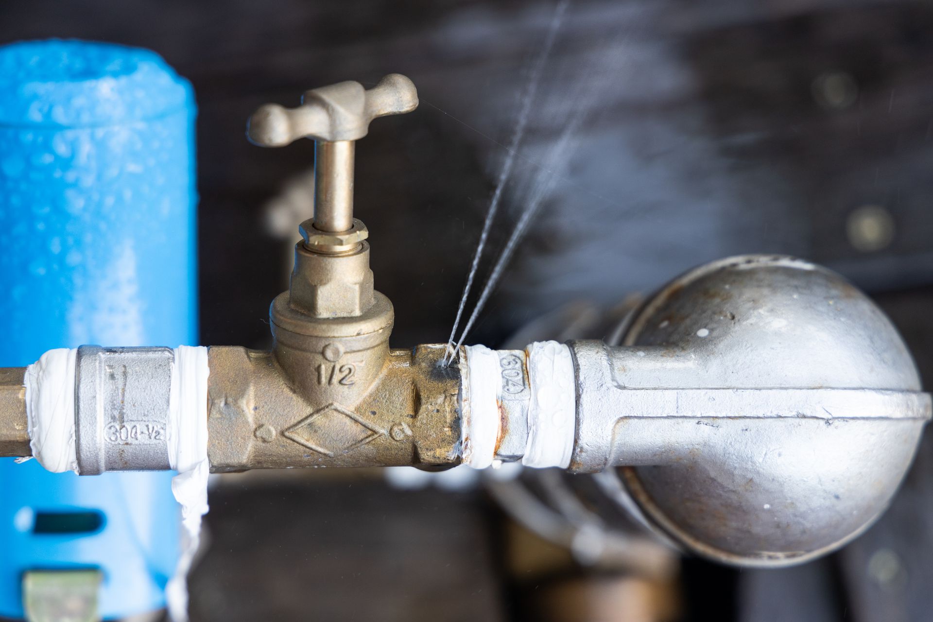 Close-up of a brass valve with a silver float on a pipe, spraying water outdoors