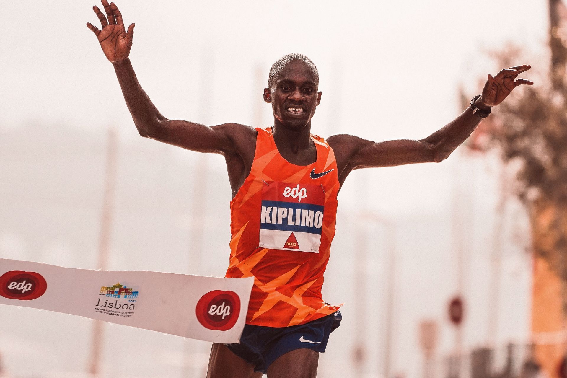 Runner in orange jersey crossing finish line with arms raised in victory