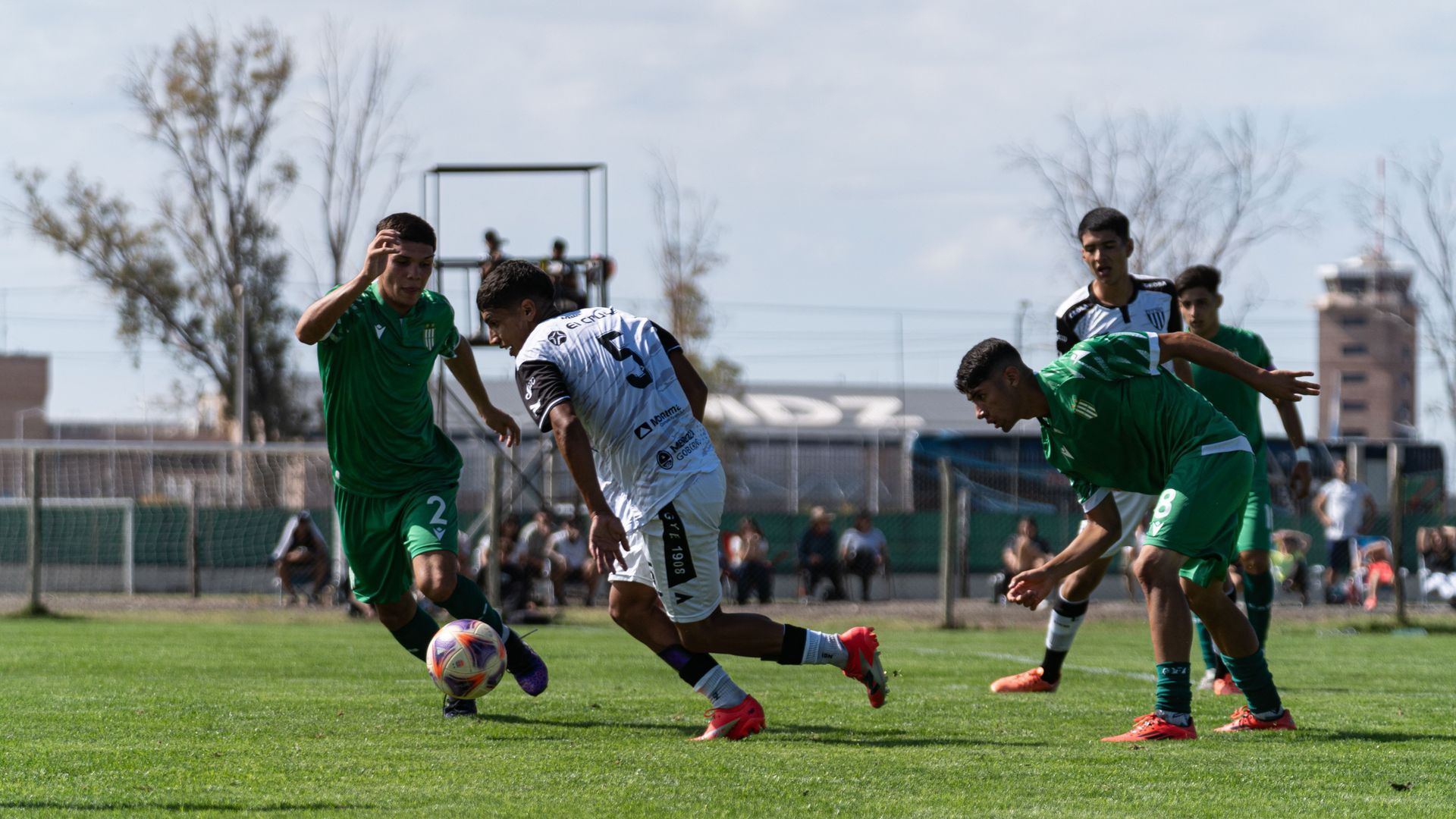 Soccer players in green and white compete for the ball on a sunny field