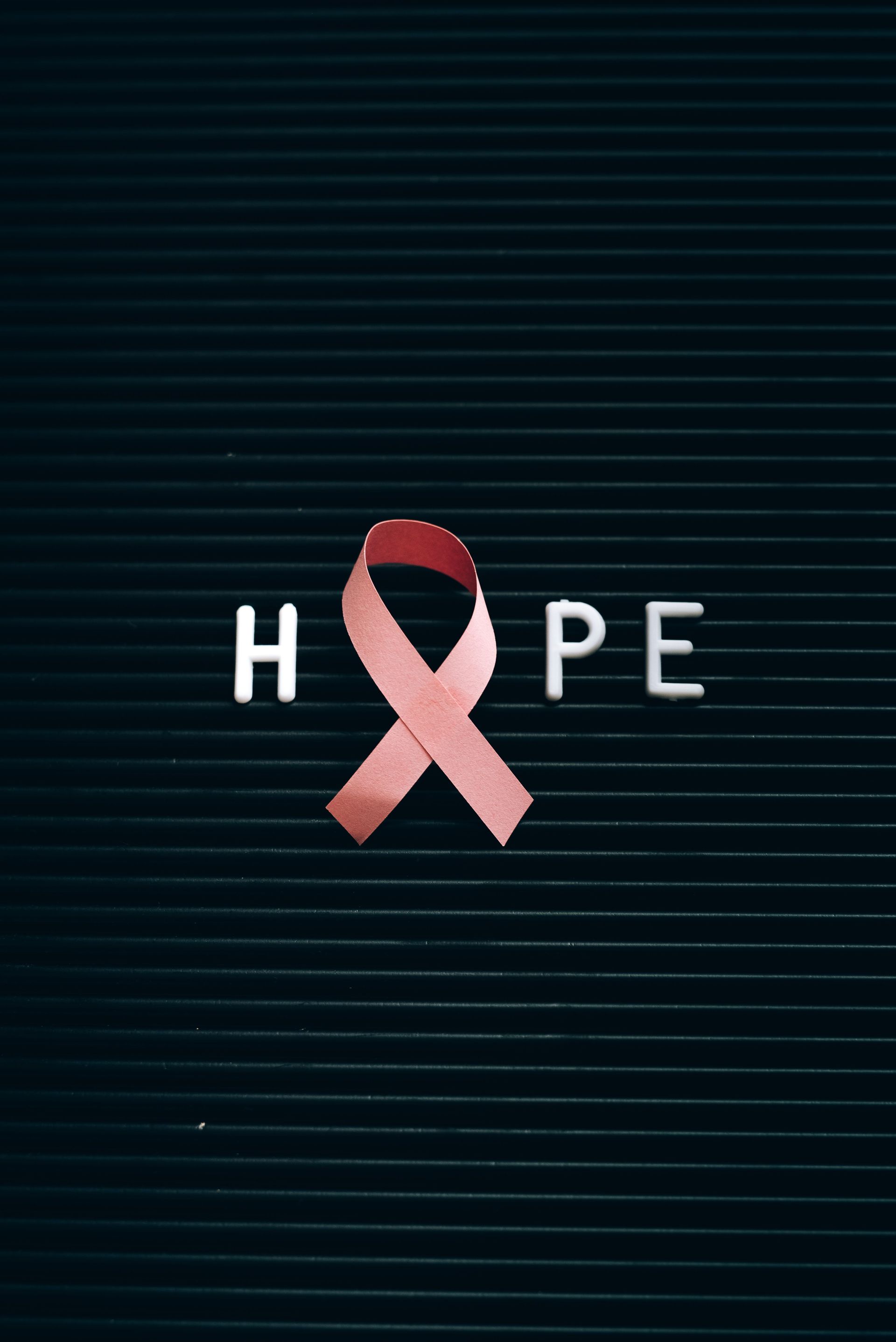 Pink breast cancer awareness ribbon replacing the “P” in HOPE on a dark striped background