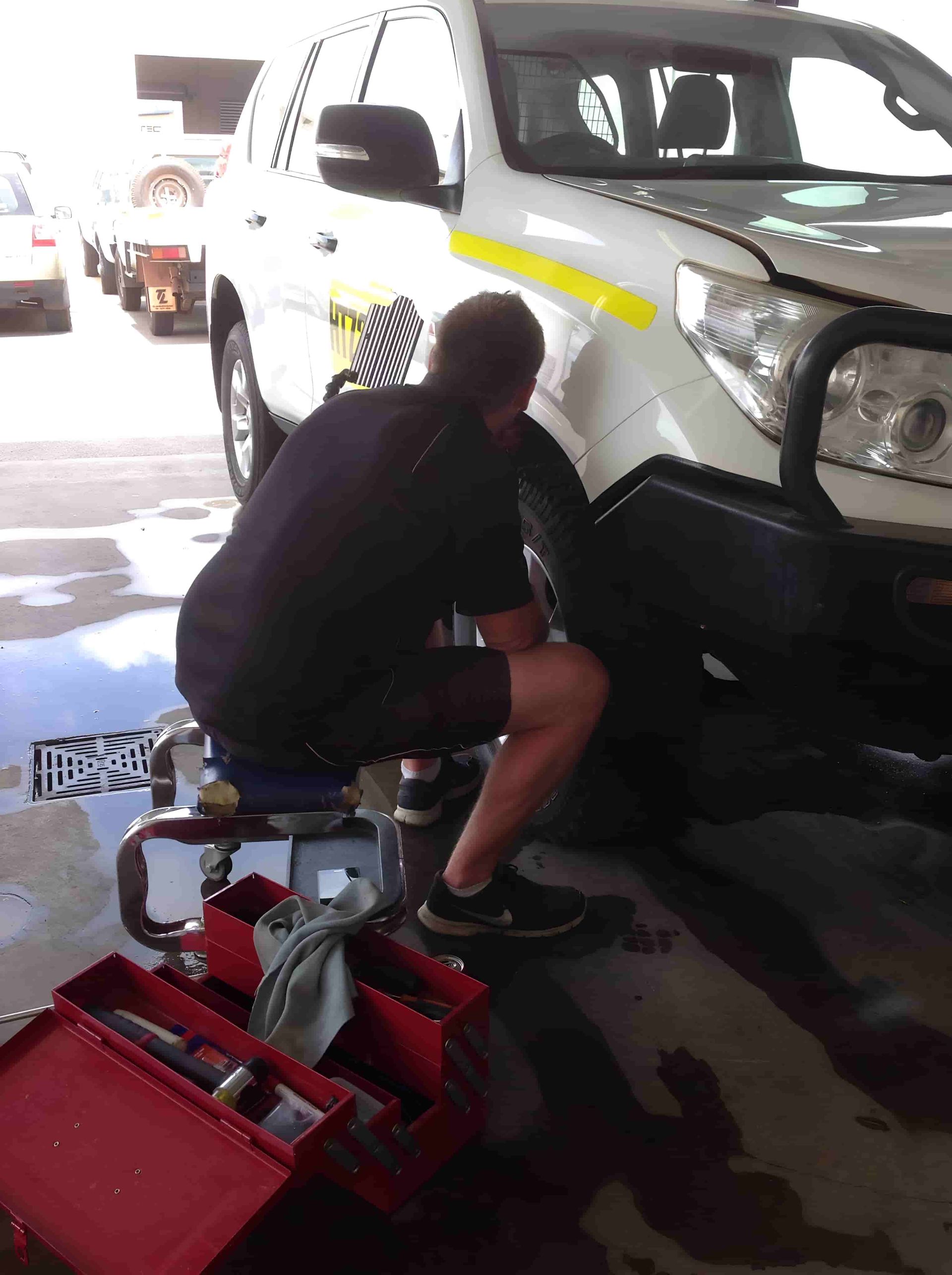 A Man is Working on a White Vehicle in a Garage — Dek-A-Dent Townsville In Wulguru, QLD