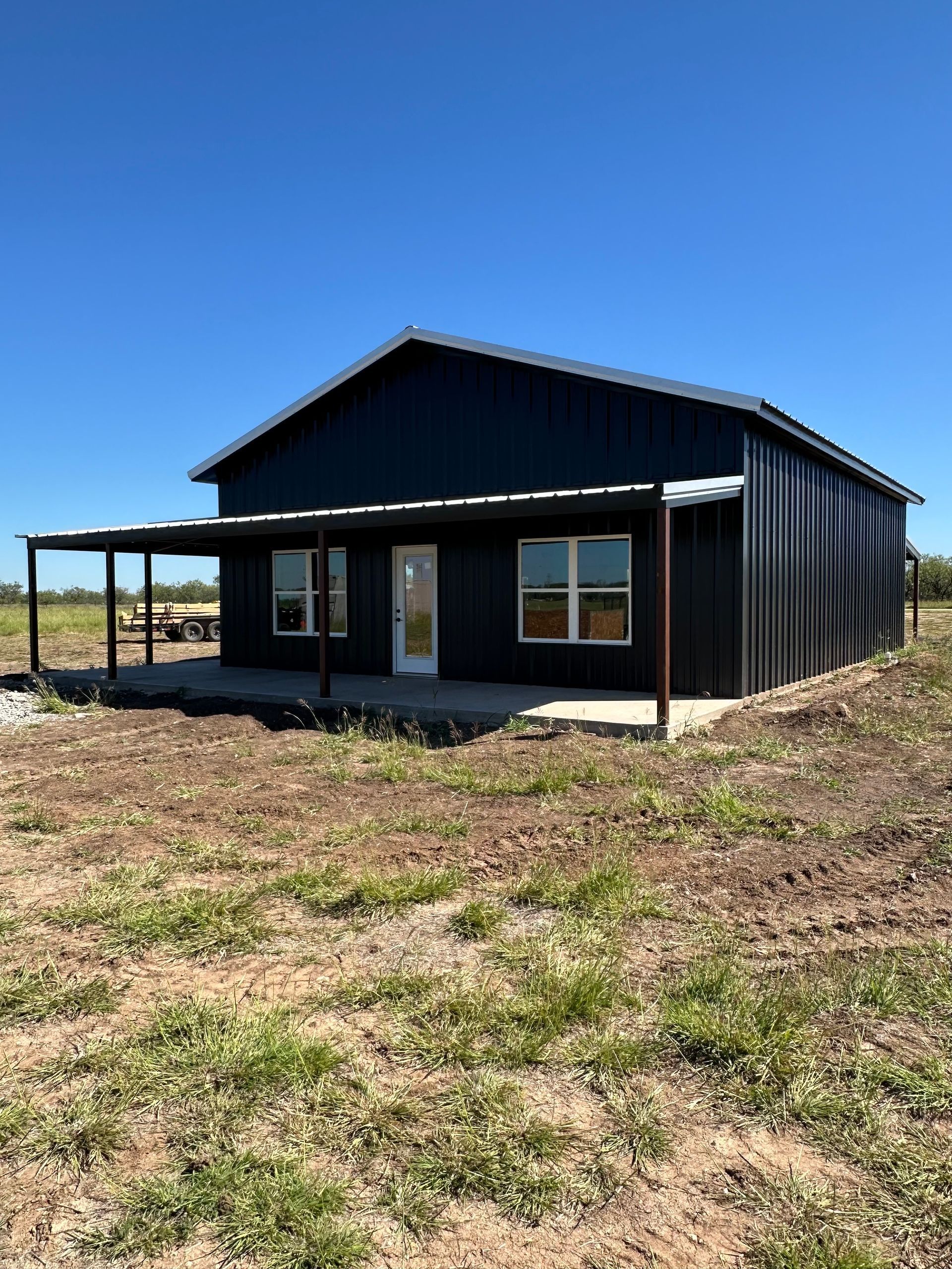 Black metal house with a covered porch in a dry, open field under a clear blue sky