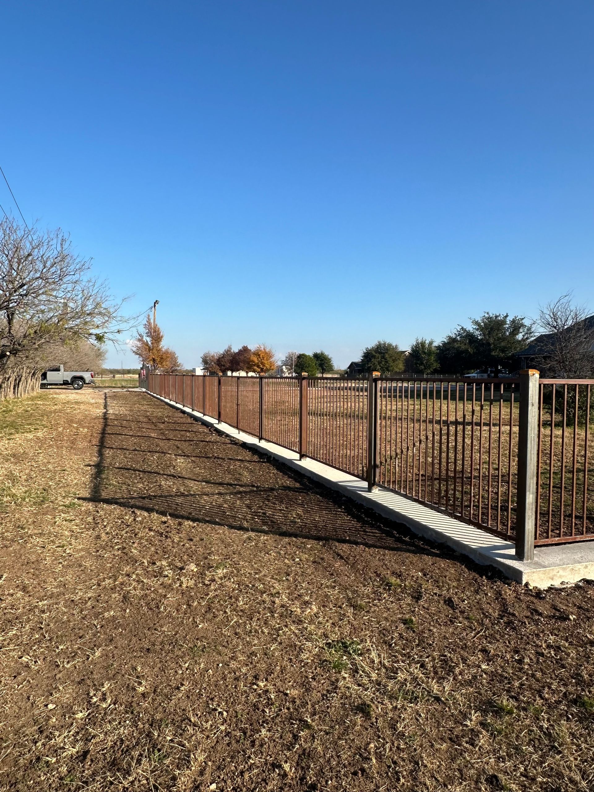 Long metal fence along a leaf-covered path under a clear blue sky