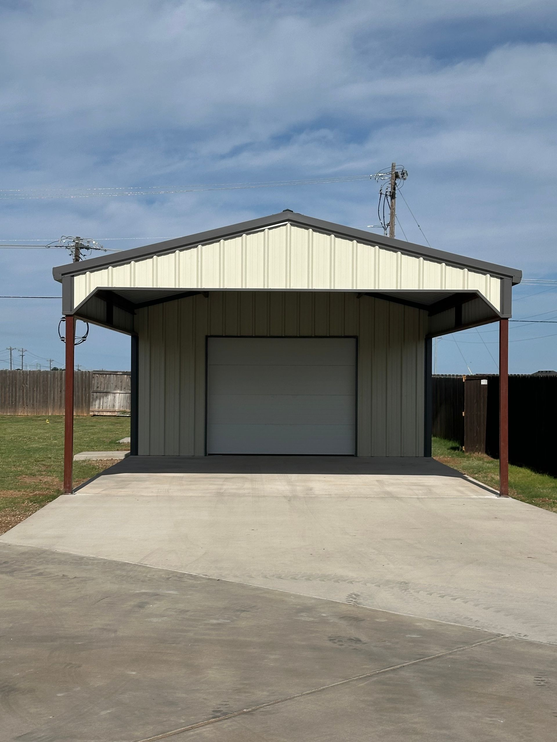 Small metal shed with a closed roll-up door, concrete ramp, and chain-link fence under a cloudy sky