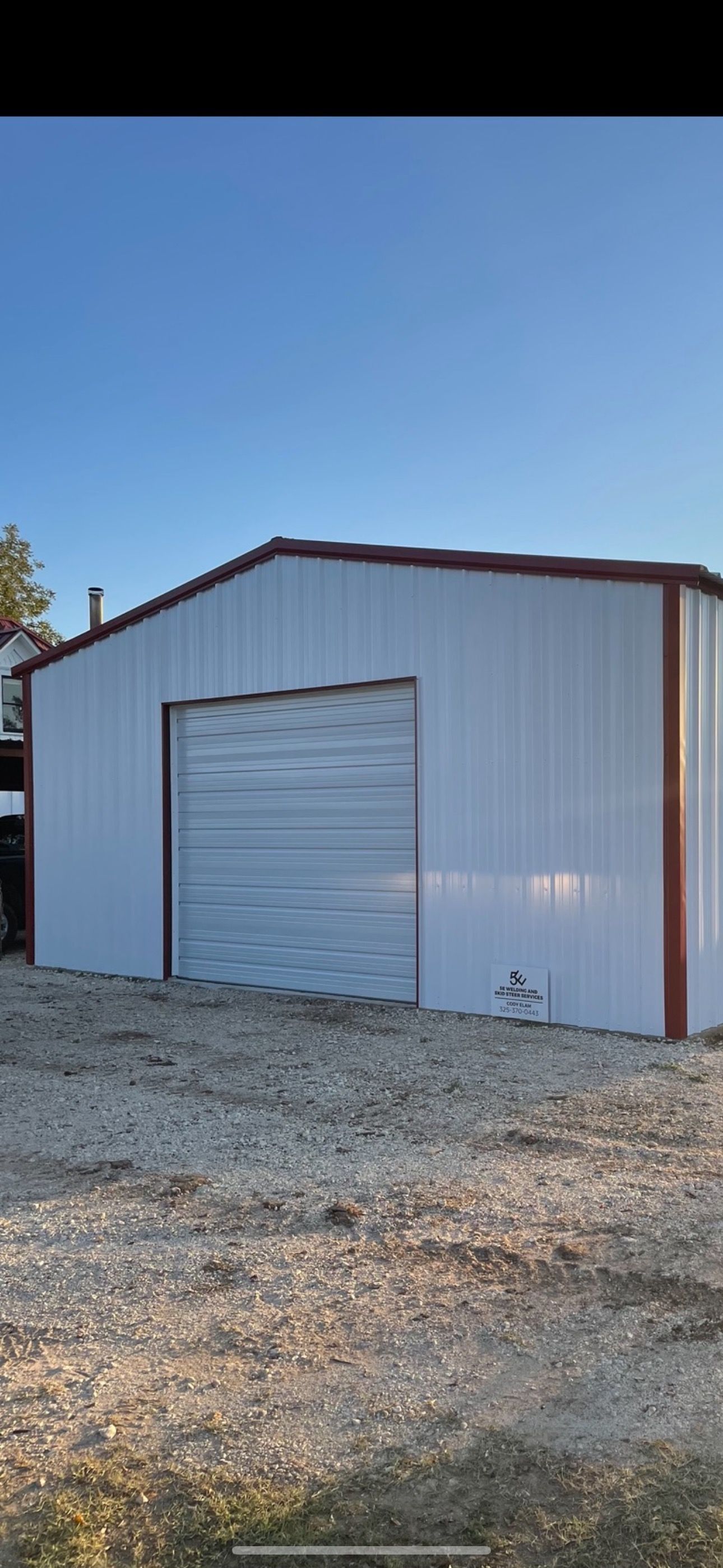 White metal garage with a roll-up door on a gravel lot under a blue sky