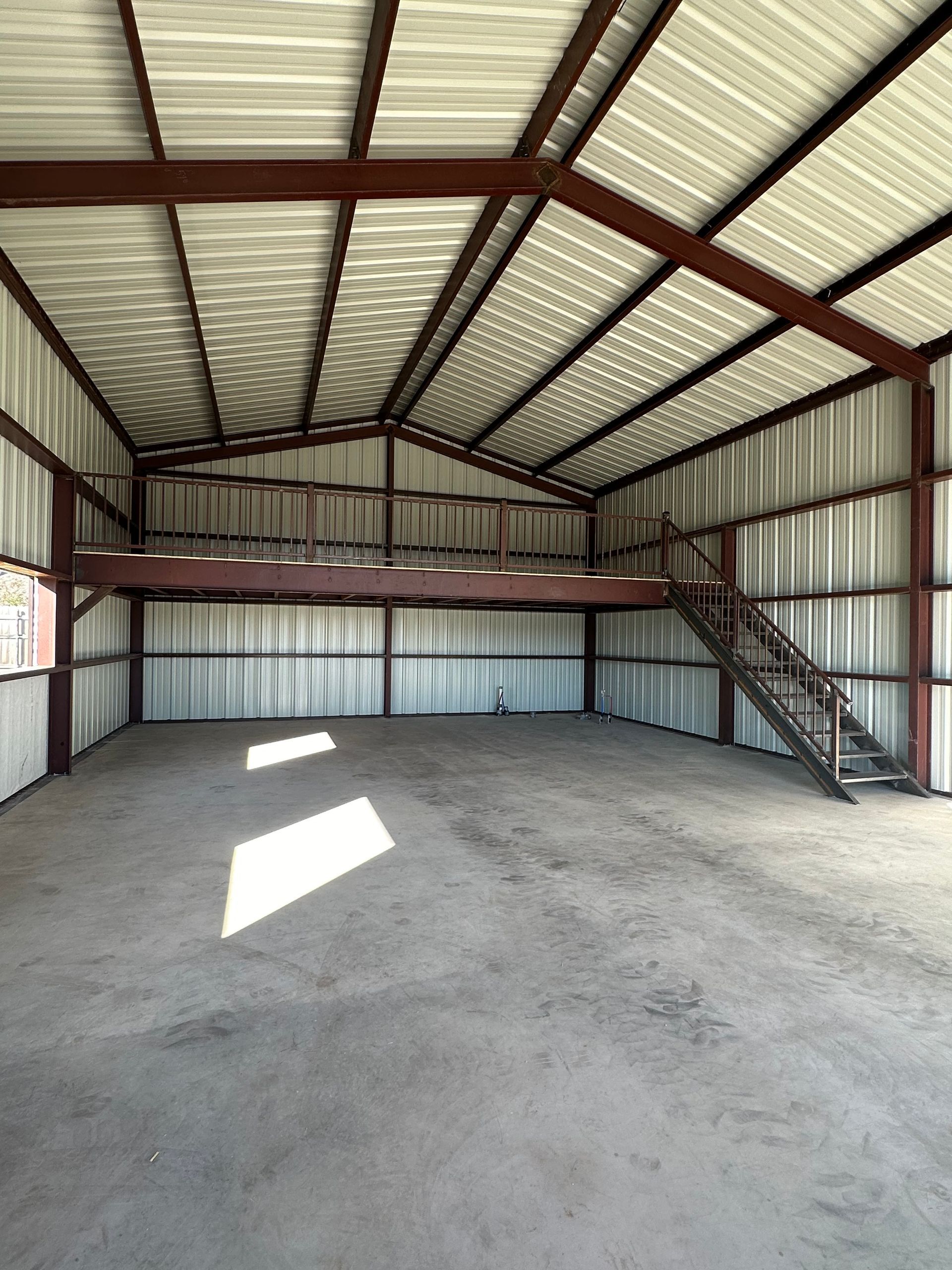 Empty metal storage shed with concrete floor and a staircase to a loft on the right.