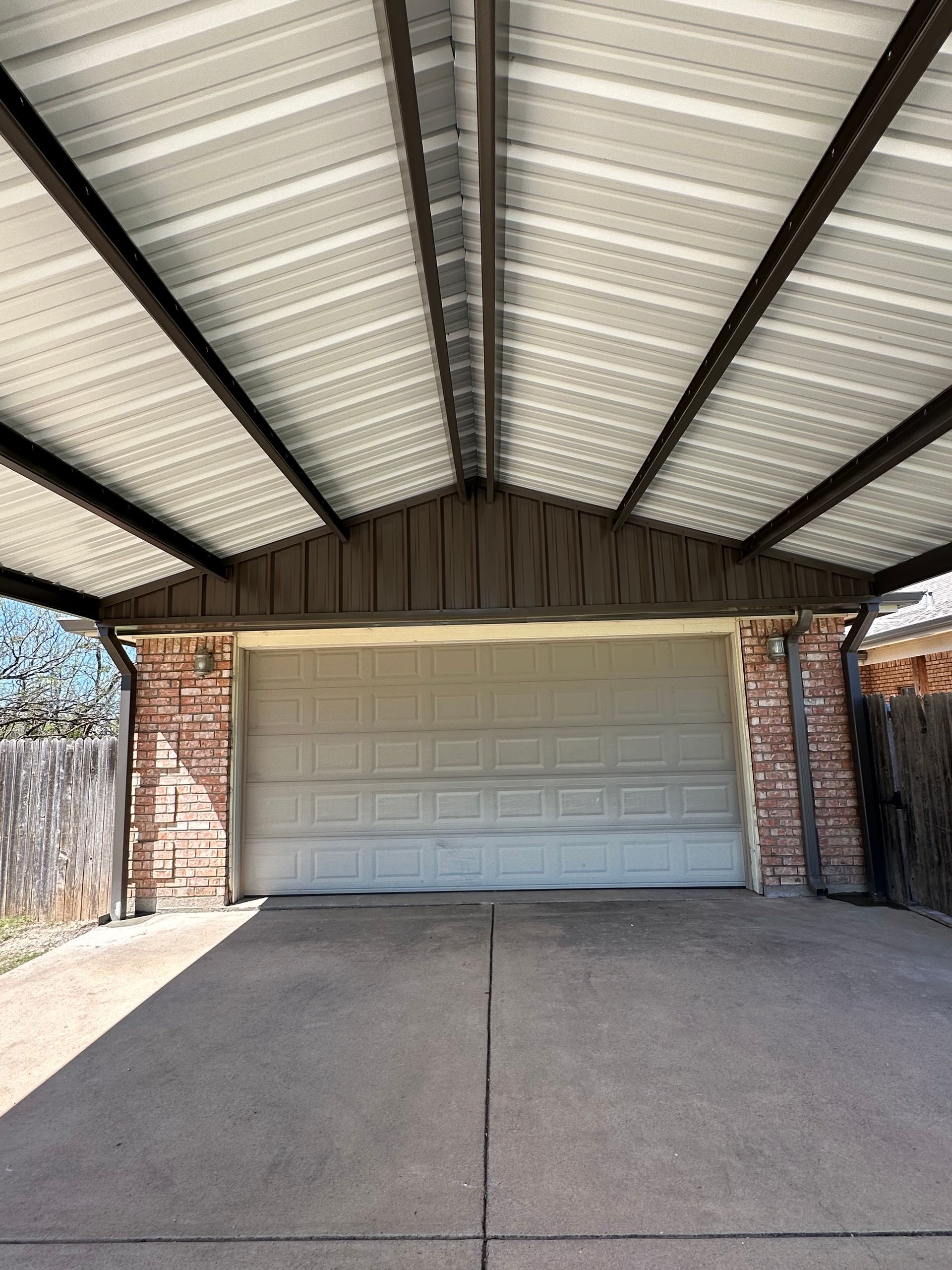Covered driveway leading to a closed beige garage door beneath a peaked roof