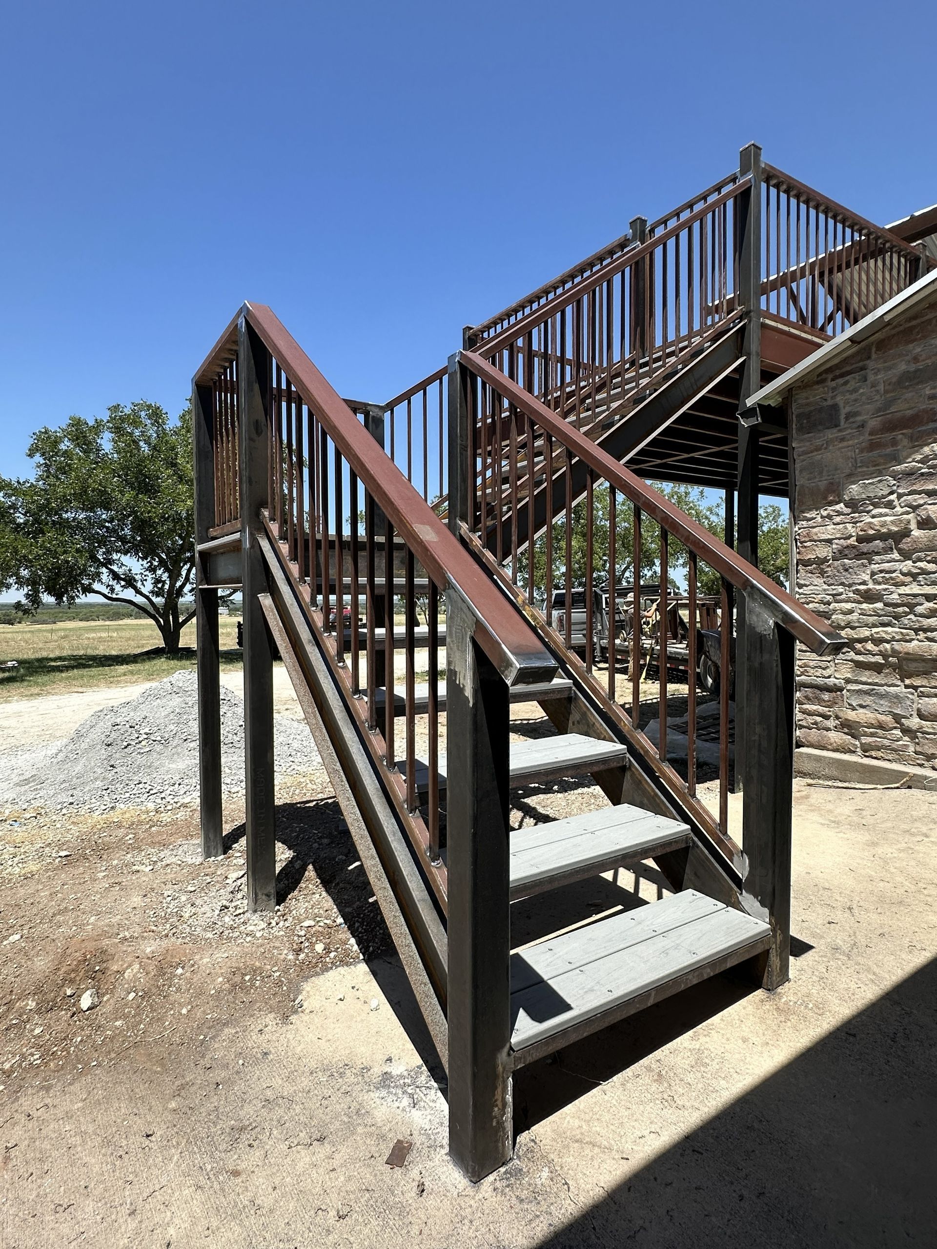 Outdoor metal staircase with wooden railings beside a stone building under a clear blue sky