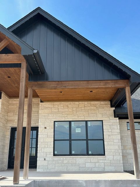 Modern house exterior with stone walls, dark blue gable, wood porch ceiling, and black-framed windows.