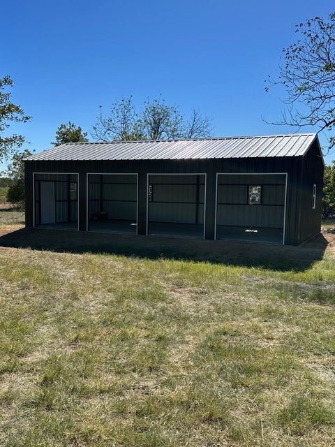 Small dark shed with a metal roof in a grassy yard under a clear blue sky