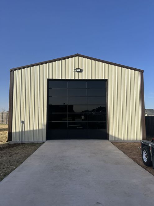 Small metal building with a large black garage door and a concrete driveway under a clear sky.