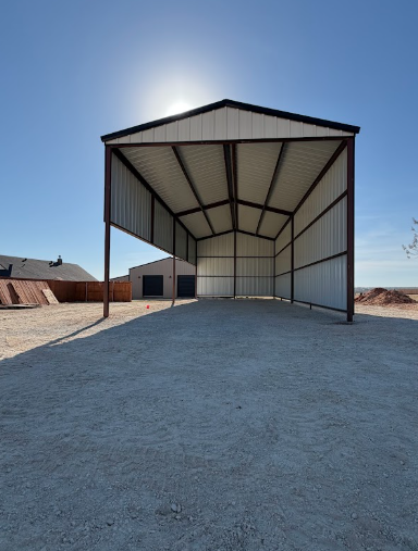 Large open-sided metal shed on a gravel lot under a clear blue sky.