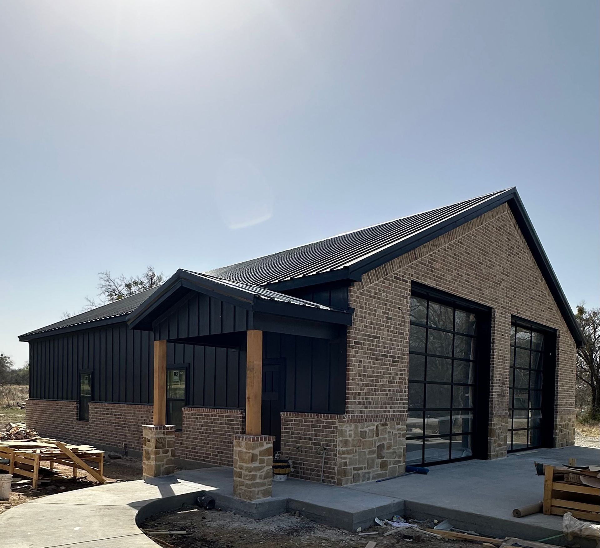 New brick house with dark siding, black roof, and large garage doors under construction