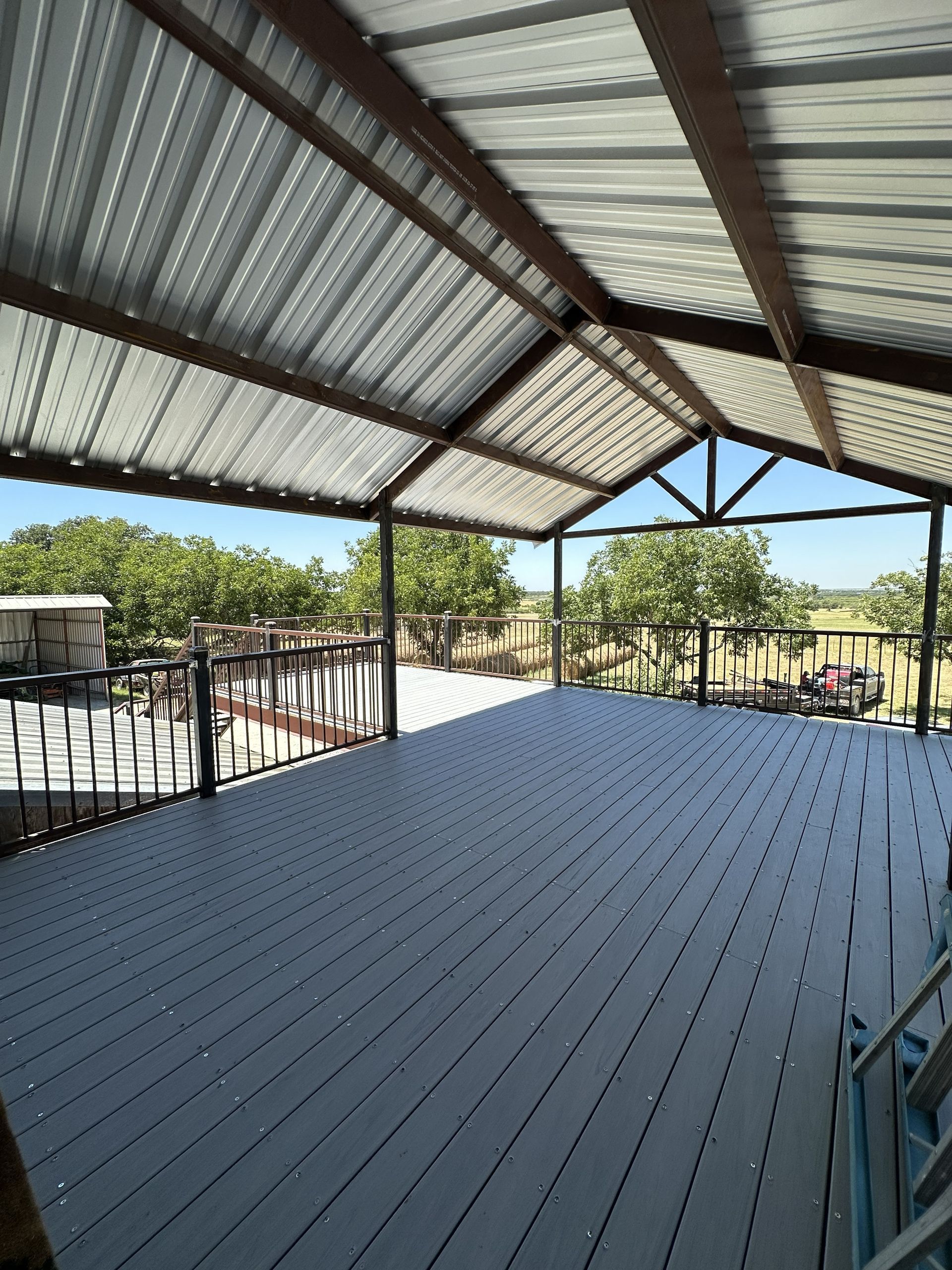 Covered outdoor patio with corrugated metal roof, gray deck, and views of trees and sky