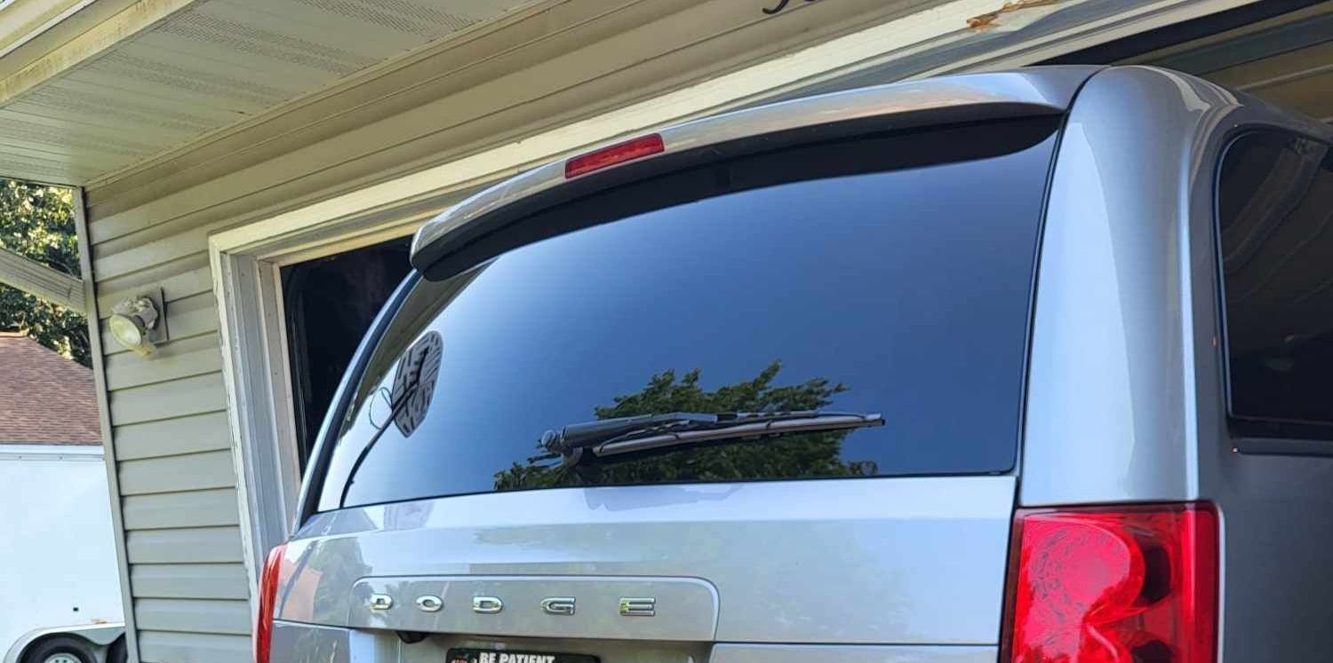 A silver minivan is parked in a garage next to a house.