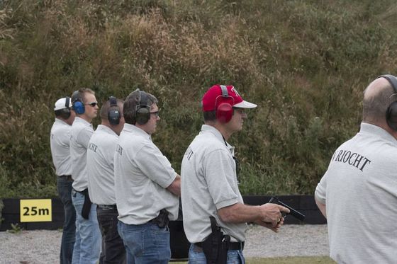 People at a shooting range: men in ear protection and white shirts.