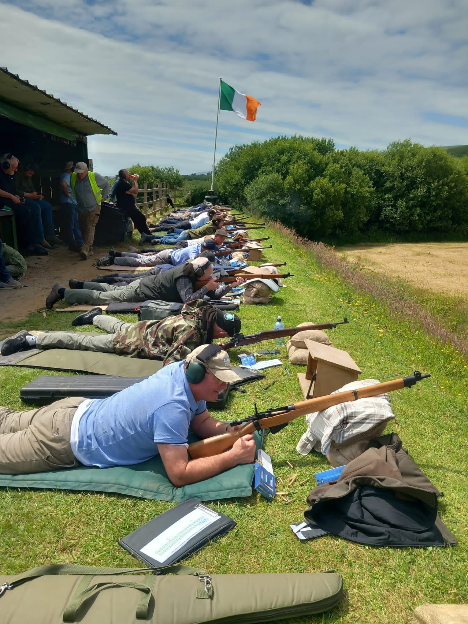 People lying prone, shooting rifles on a grassy range, under an Irish flag.