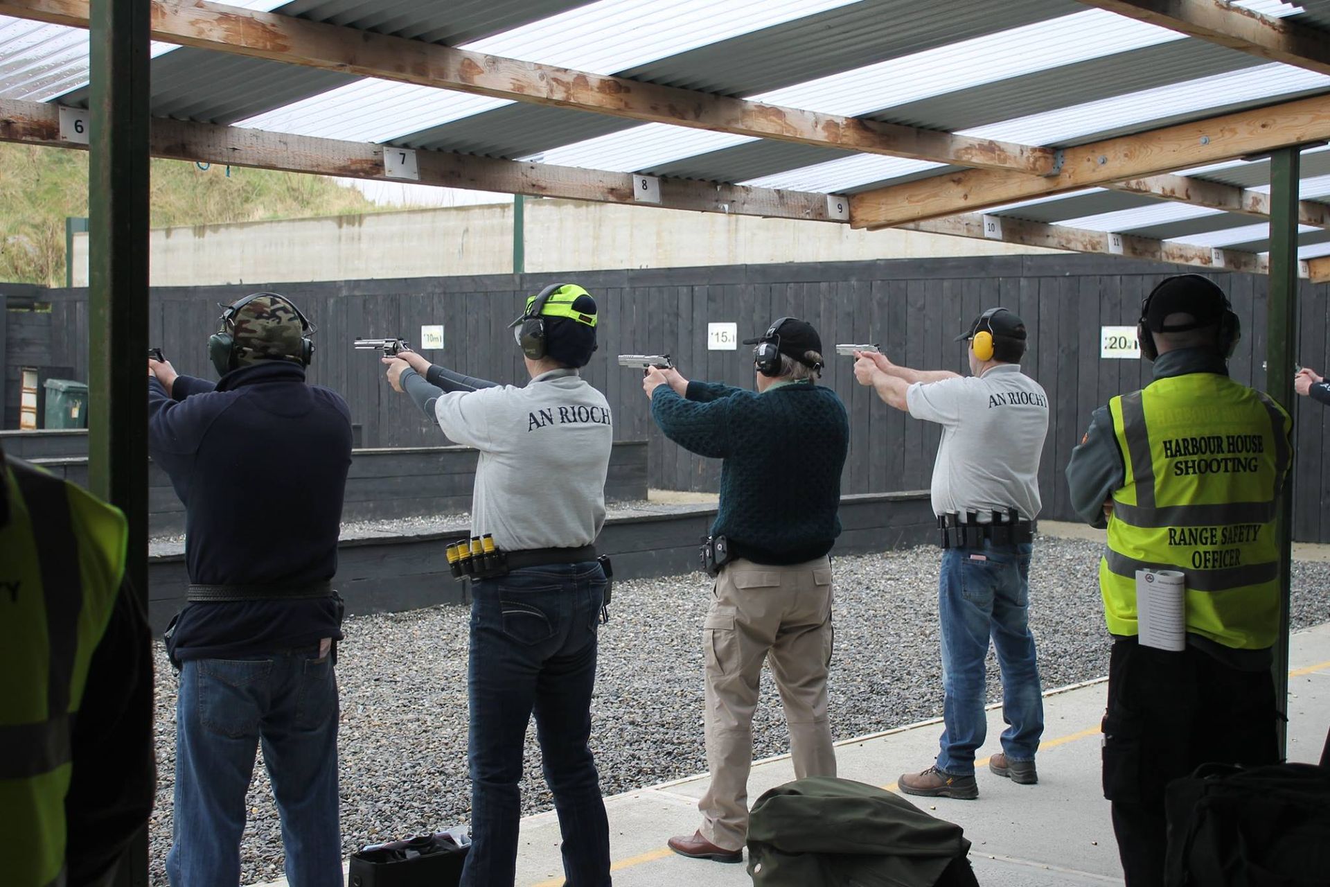 People shooting handguns at a shooting range. They are wearing eye and ear protection, aimed at targets.