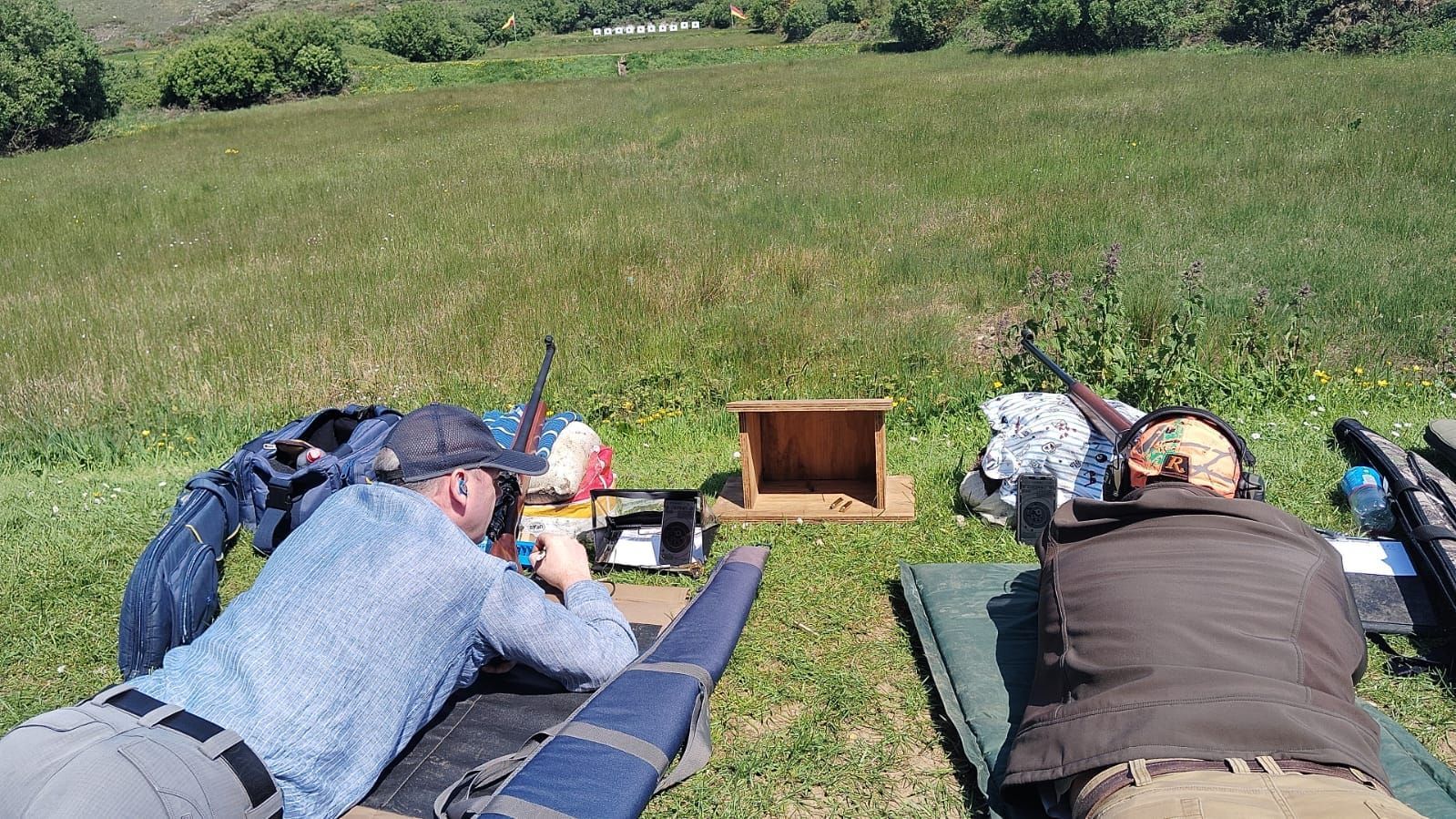 Two people aiming rifles at a target on a grassy outdoor shooting range.