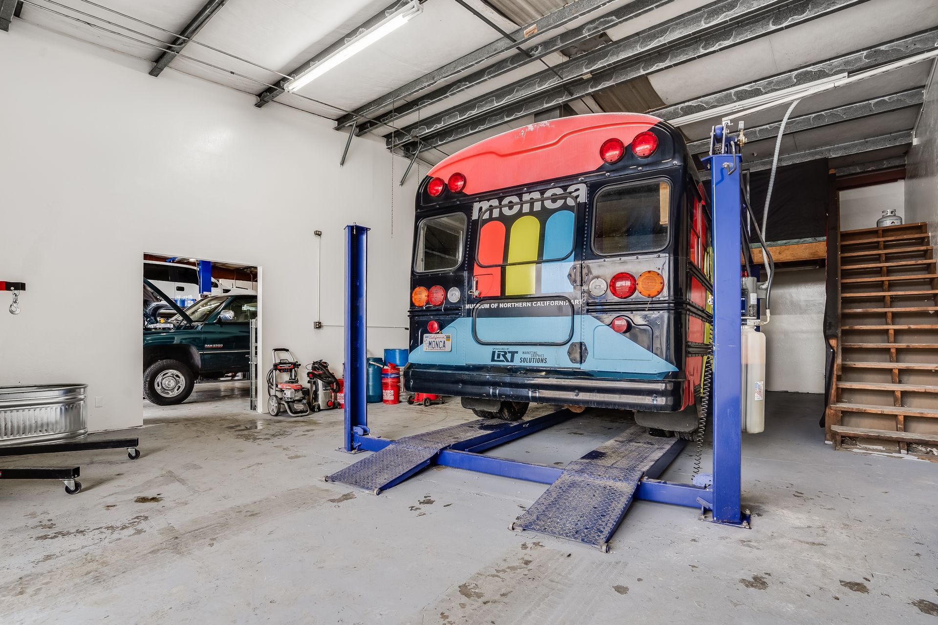 Car in a garage on a lift, rear facing camera, with tools and shelves nearby