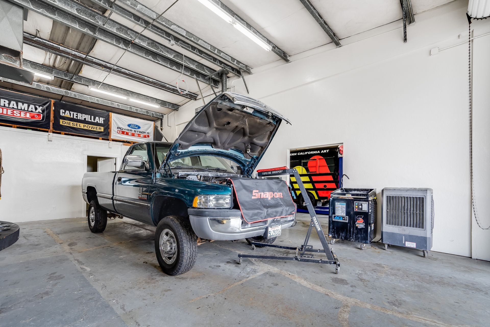 Blue pickup truck in a garage, hood open for engine work, with tools and equipment nearby