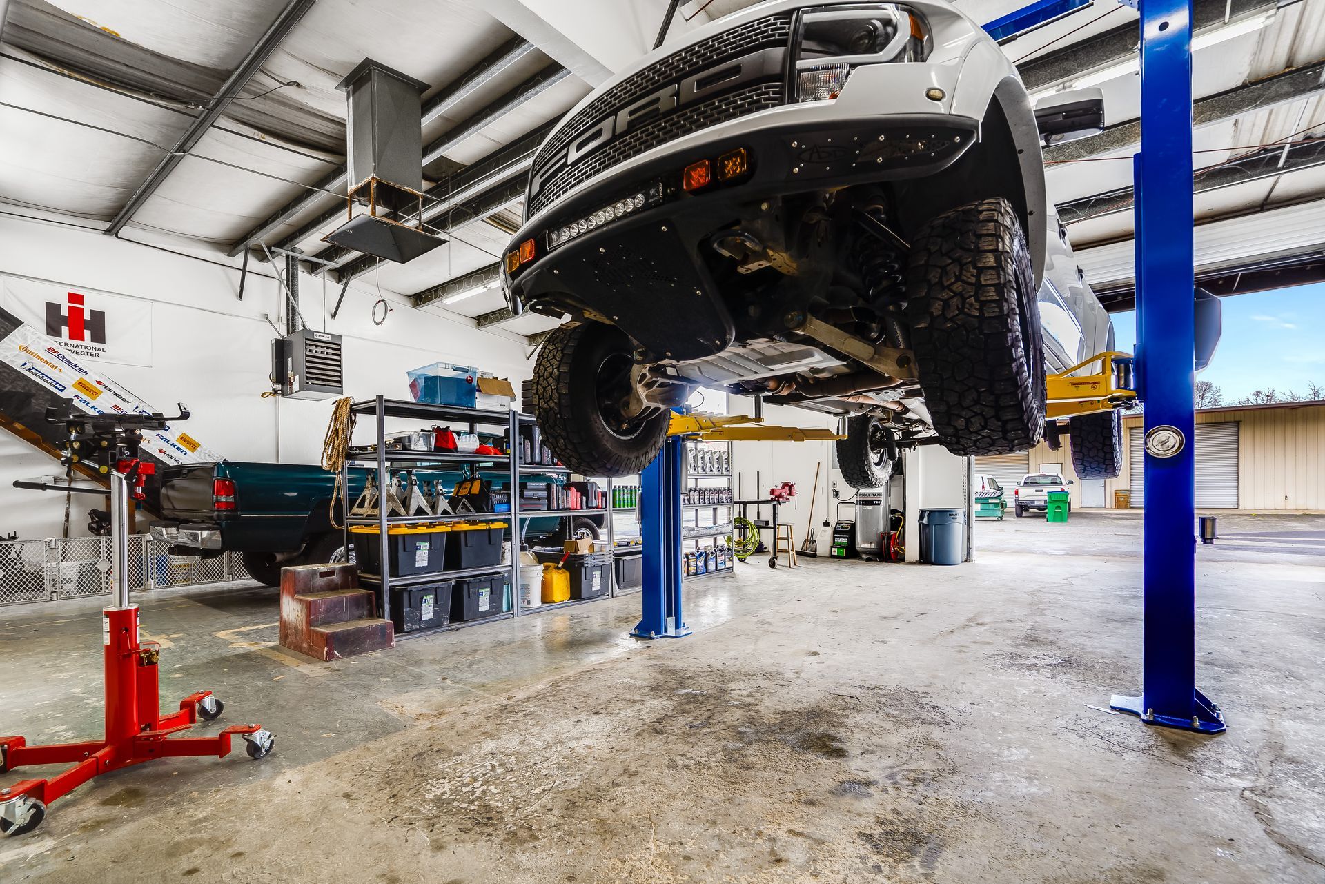 Car lifted on blue hydraulic posts in an auto repair garage, with tools and equipment nearby.