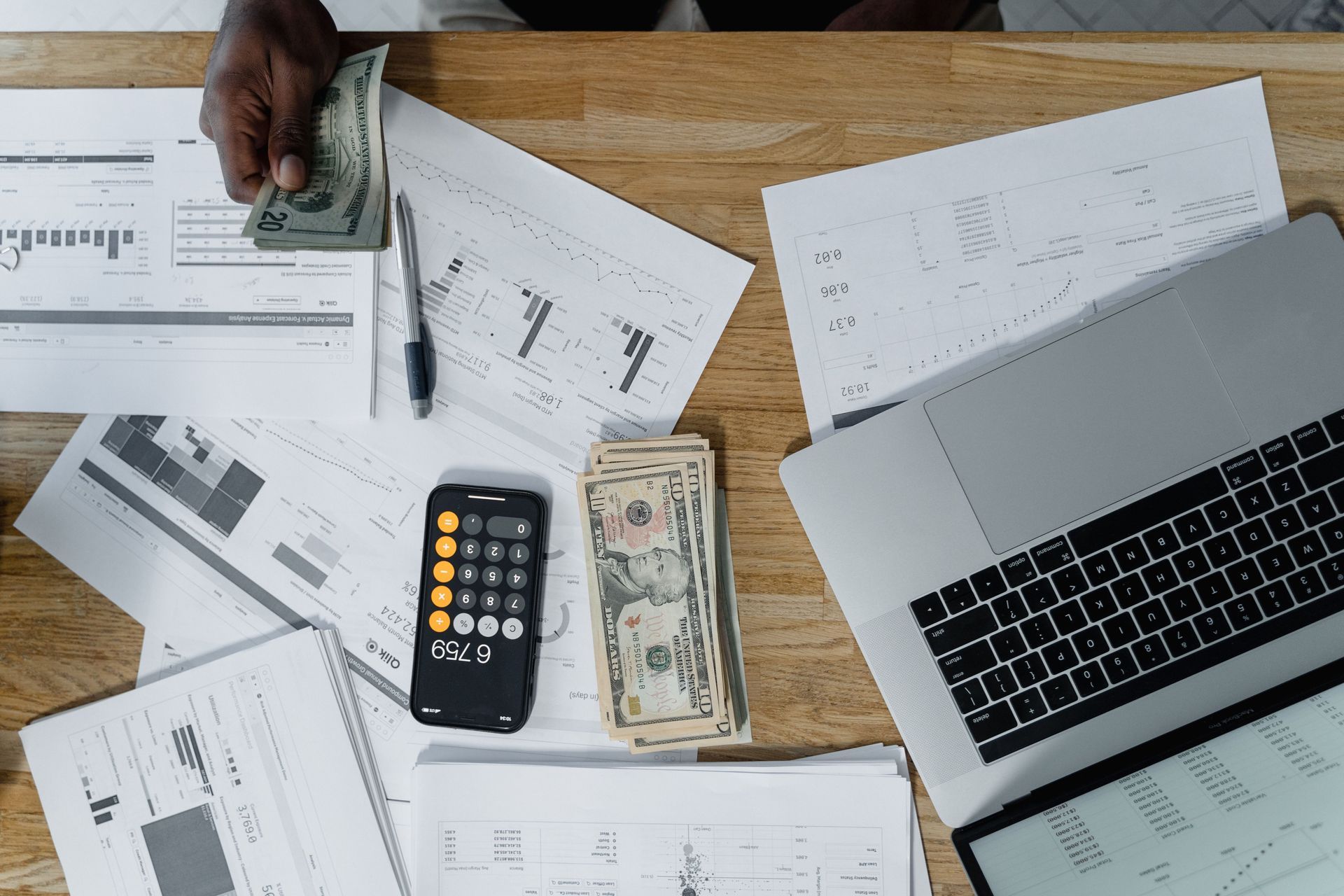Overhead view of a desk with papers, calculator, cash, and an open laptop