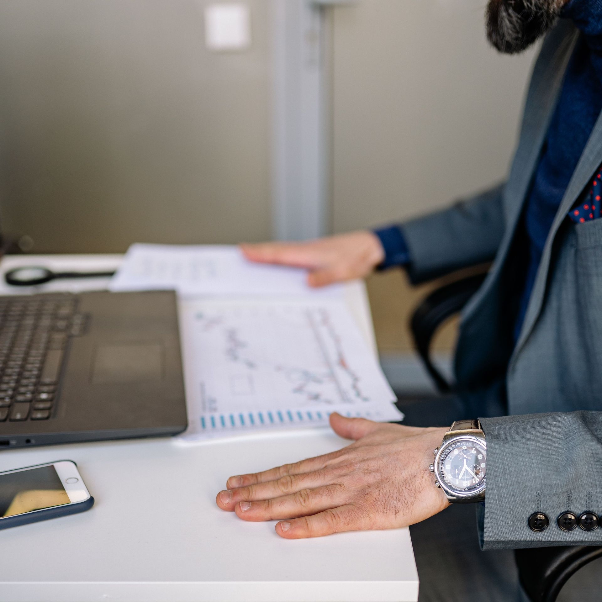 Person in a gray suit reviewing charts at a desk with a laptop and smartphone