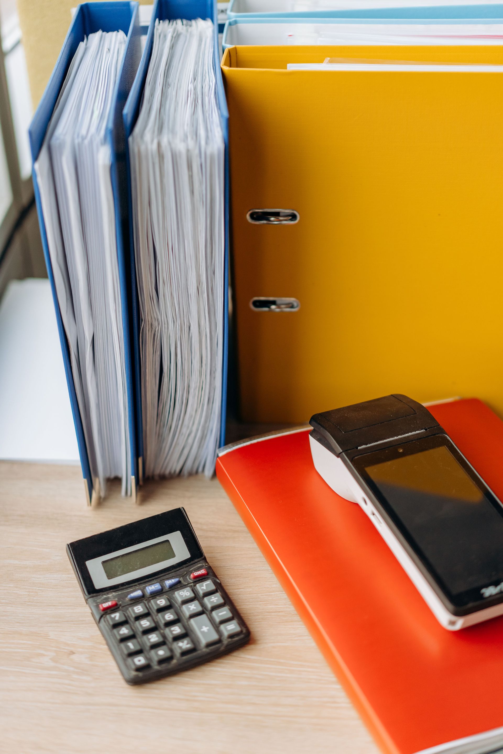 Desk with colorful binders, calculator, and smartphone on a notebook.