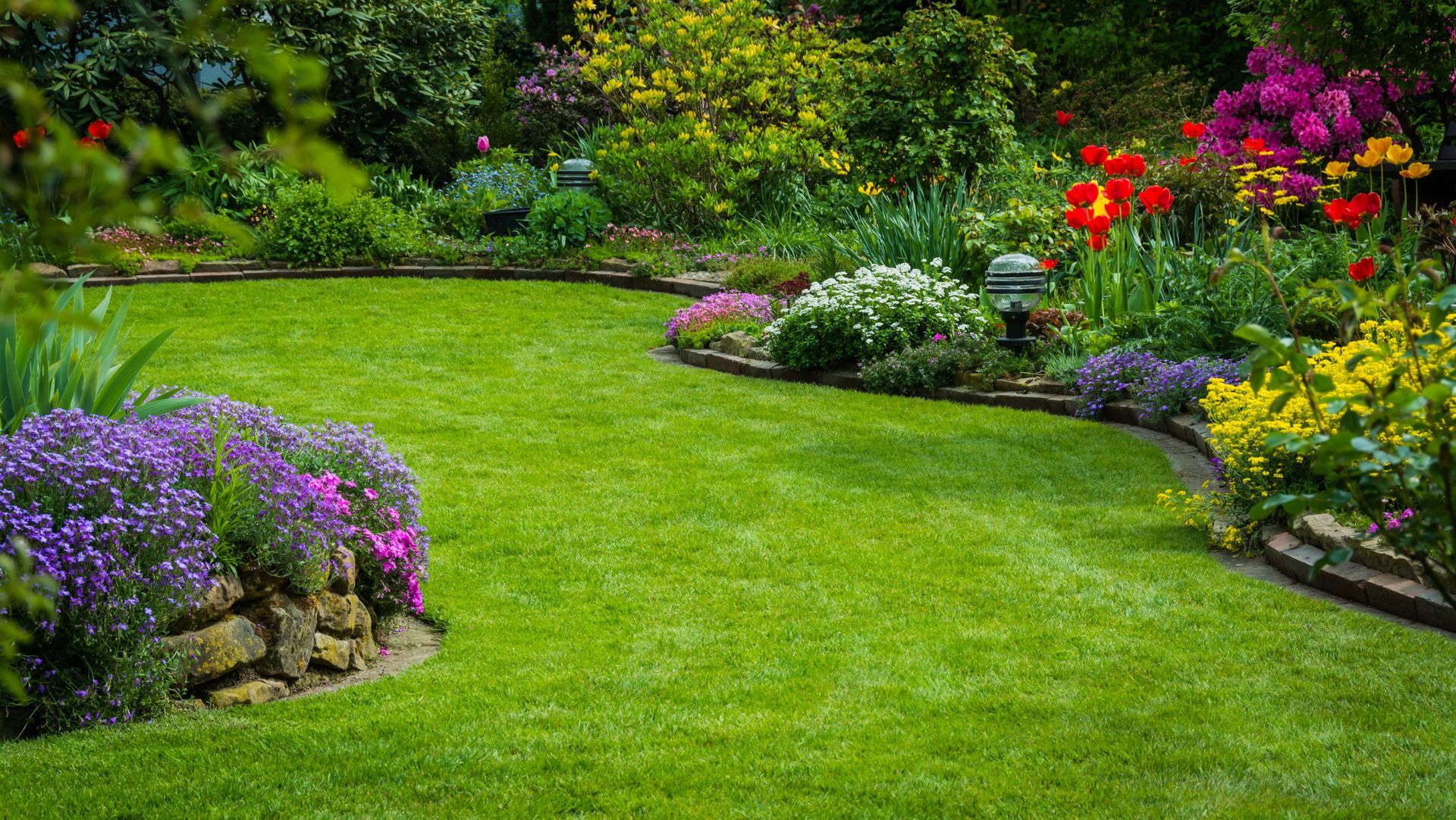 Lush garden with a green lawn bordered by colorful flowering beds and shrubs