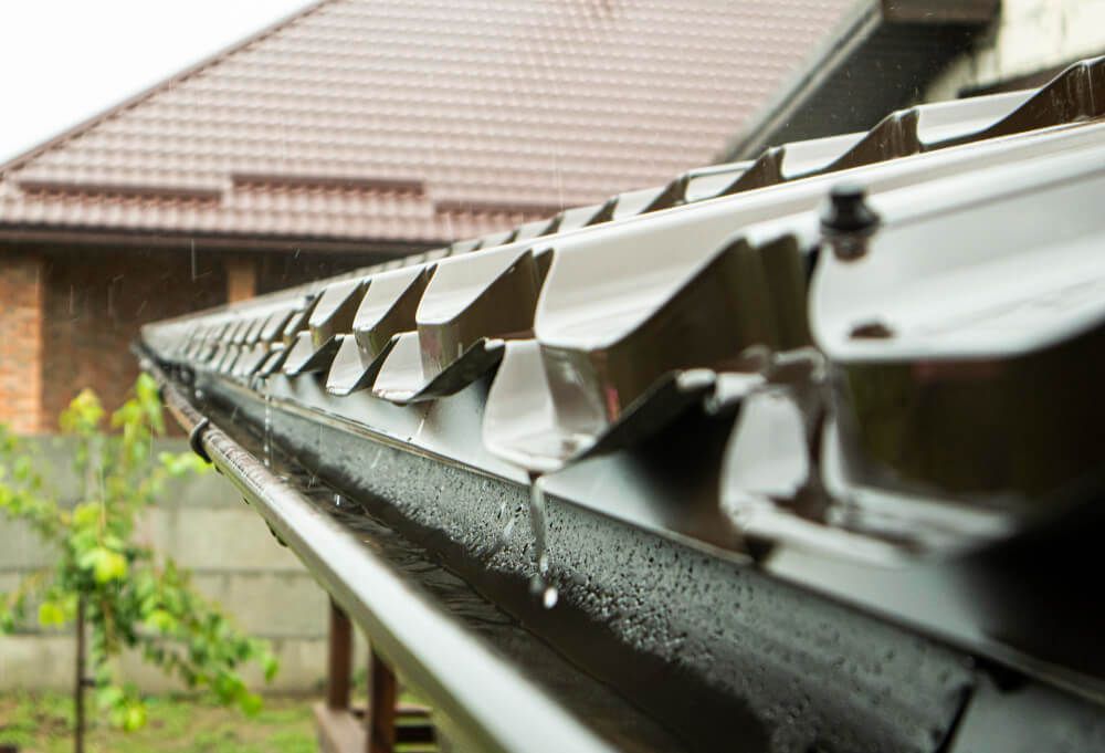 A close up of a gutter on a roof with water coming out of it.