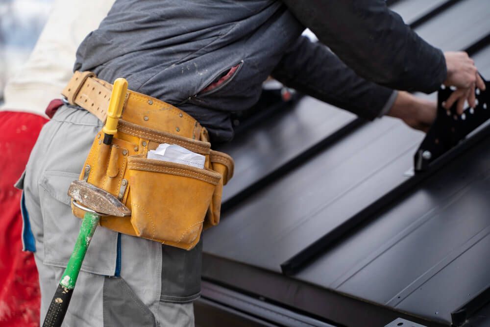 A man wearing a tool belt is working on a roof.