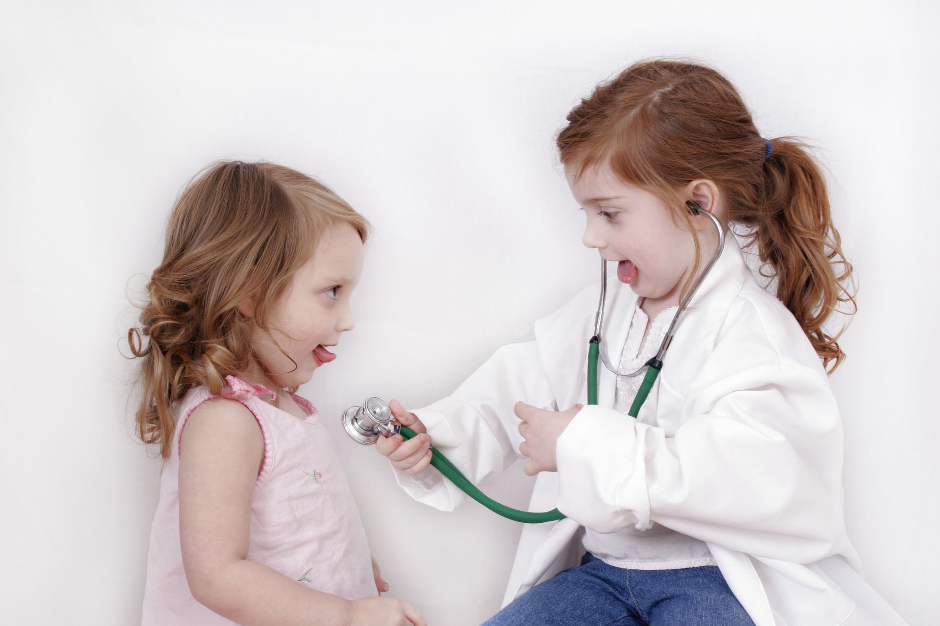 Child giving a teddy bear a checkup with a toy doctor kit against a white background
