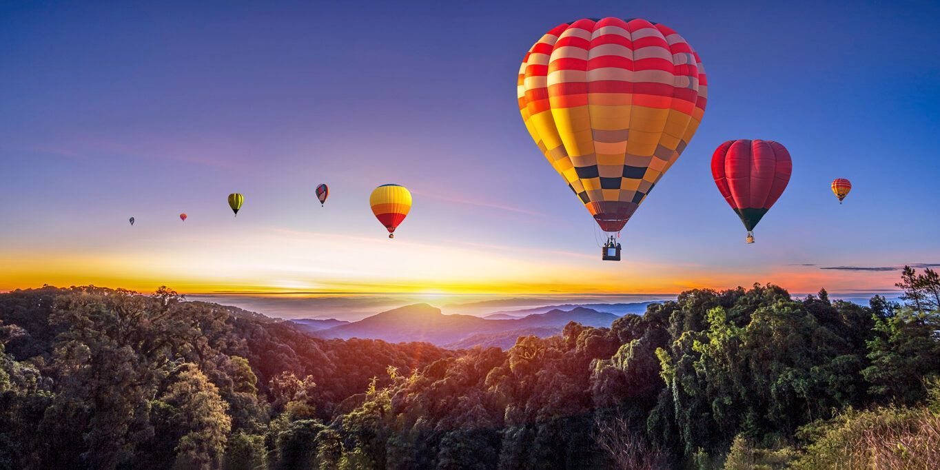 A group of hot air balloons are flying over a forest at sunset.