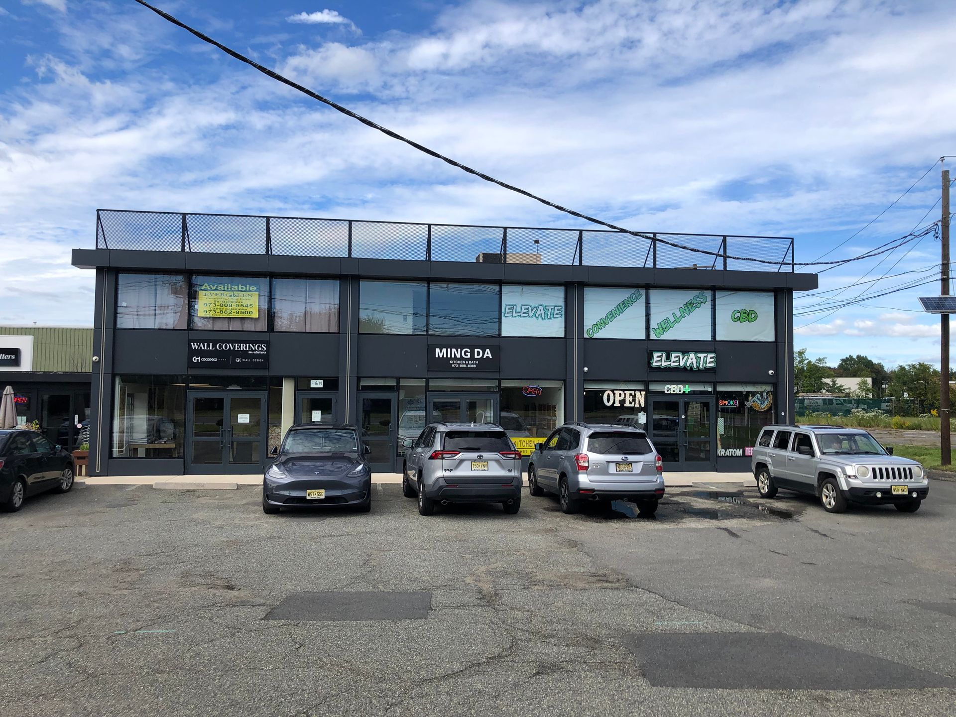 Strip mall storefront with parked cars under a cloudy sky