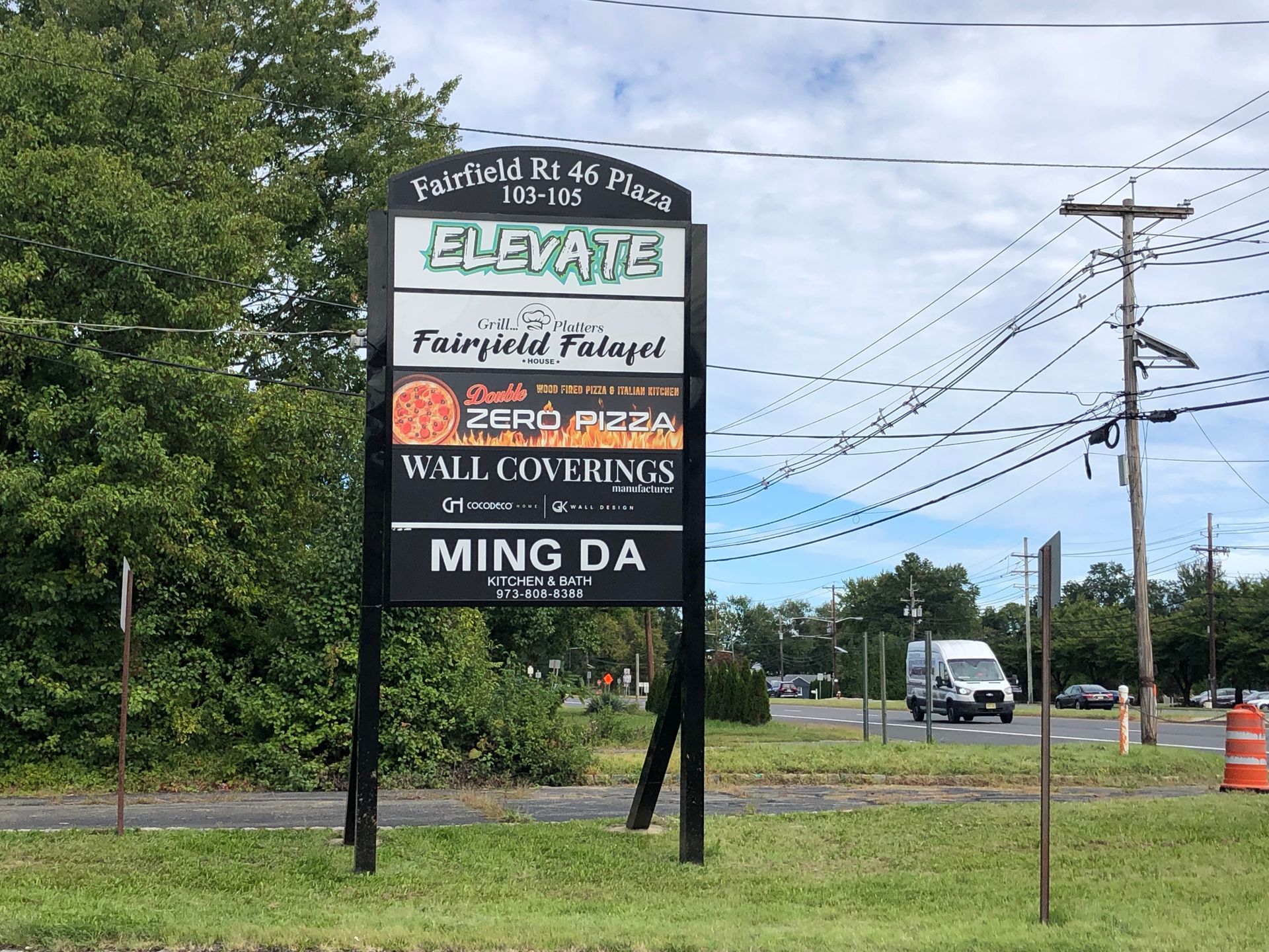 Roadside business sign for Elevators, Fayetteville, Wall Coatings, and Ming Da in a grassy lot.