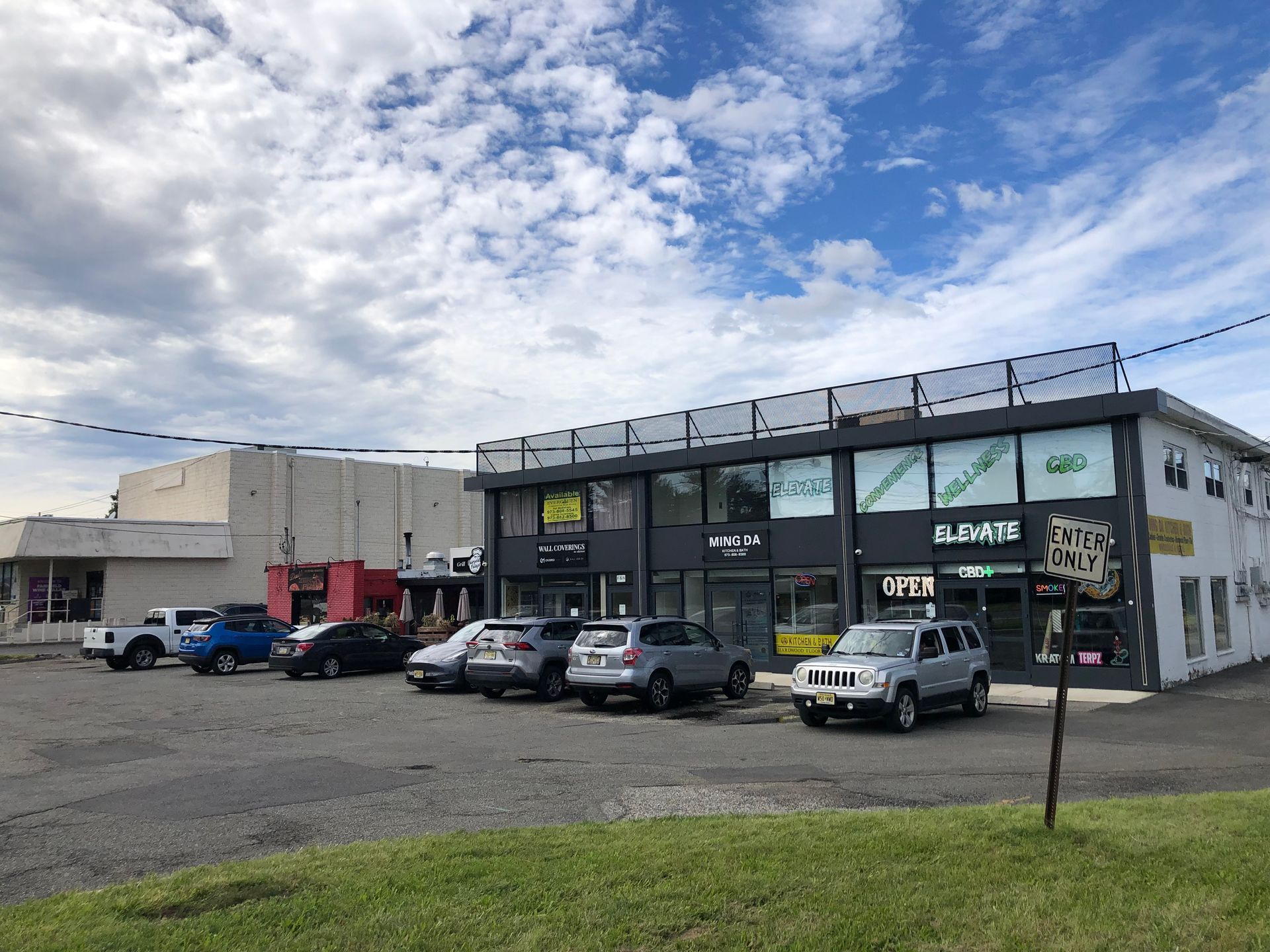 Small commercial building with parked cars in front under a cloudy blue sky