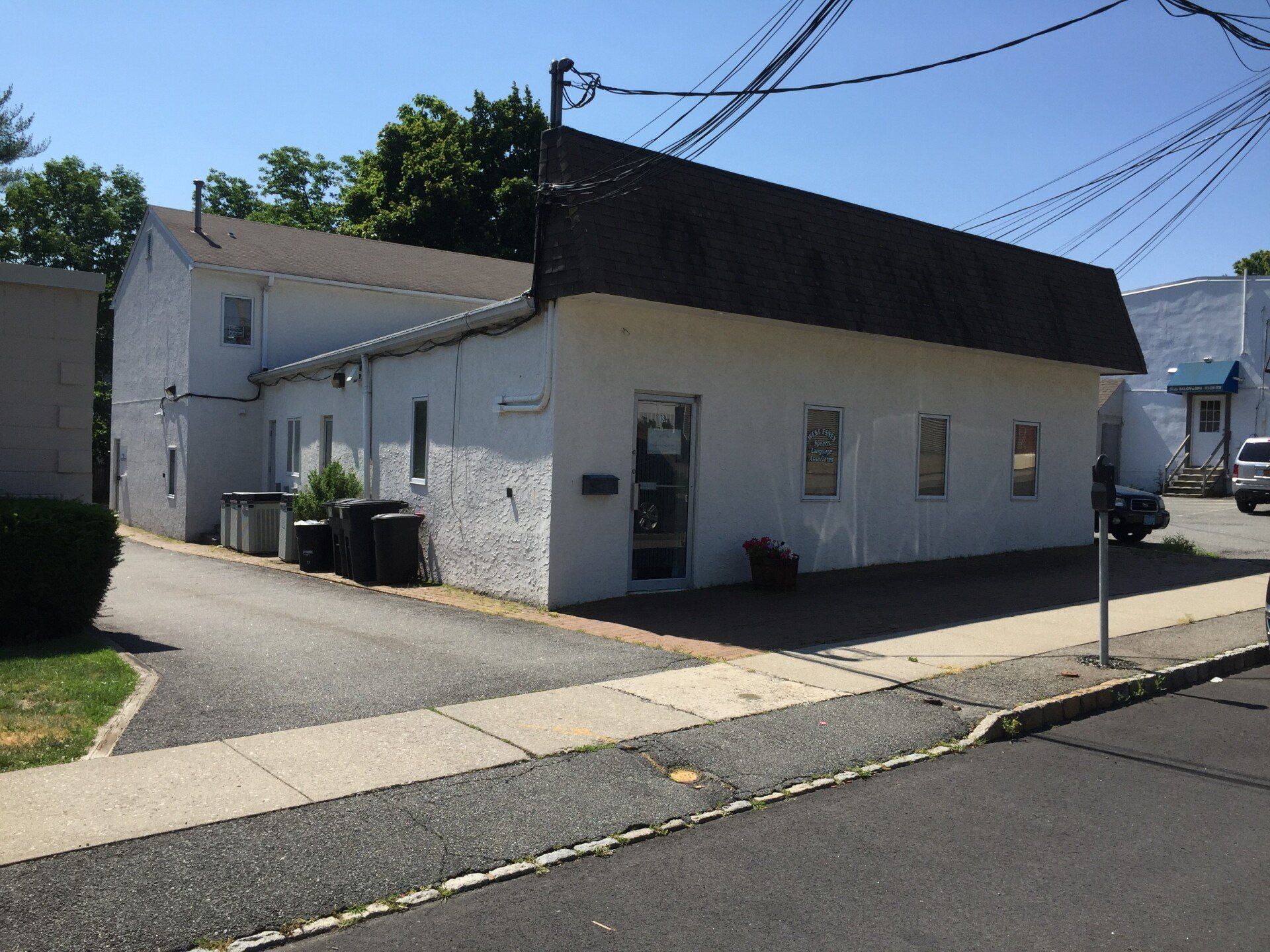 White commercial building with dark roof, small windows, and a paved driveway.