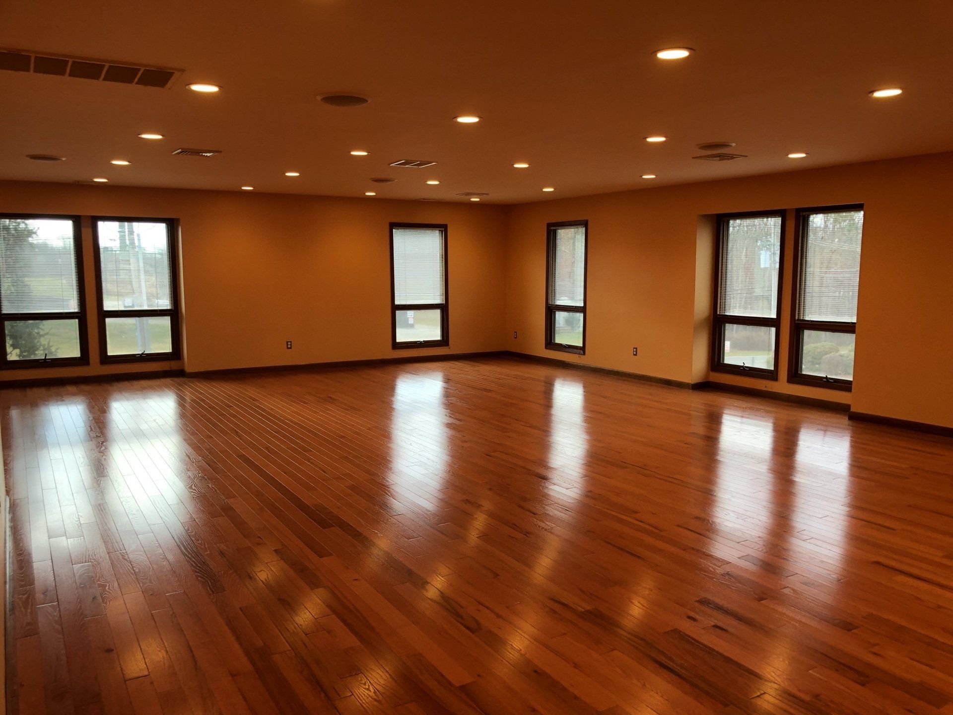 Empty room with wood floor, multiple windows, and recessed lighting.