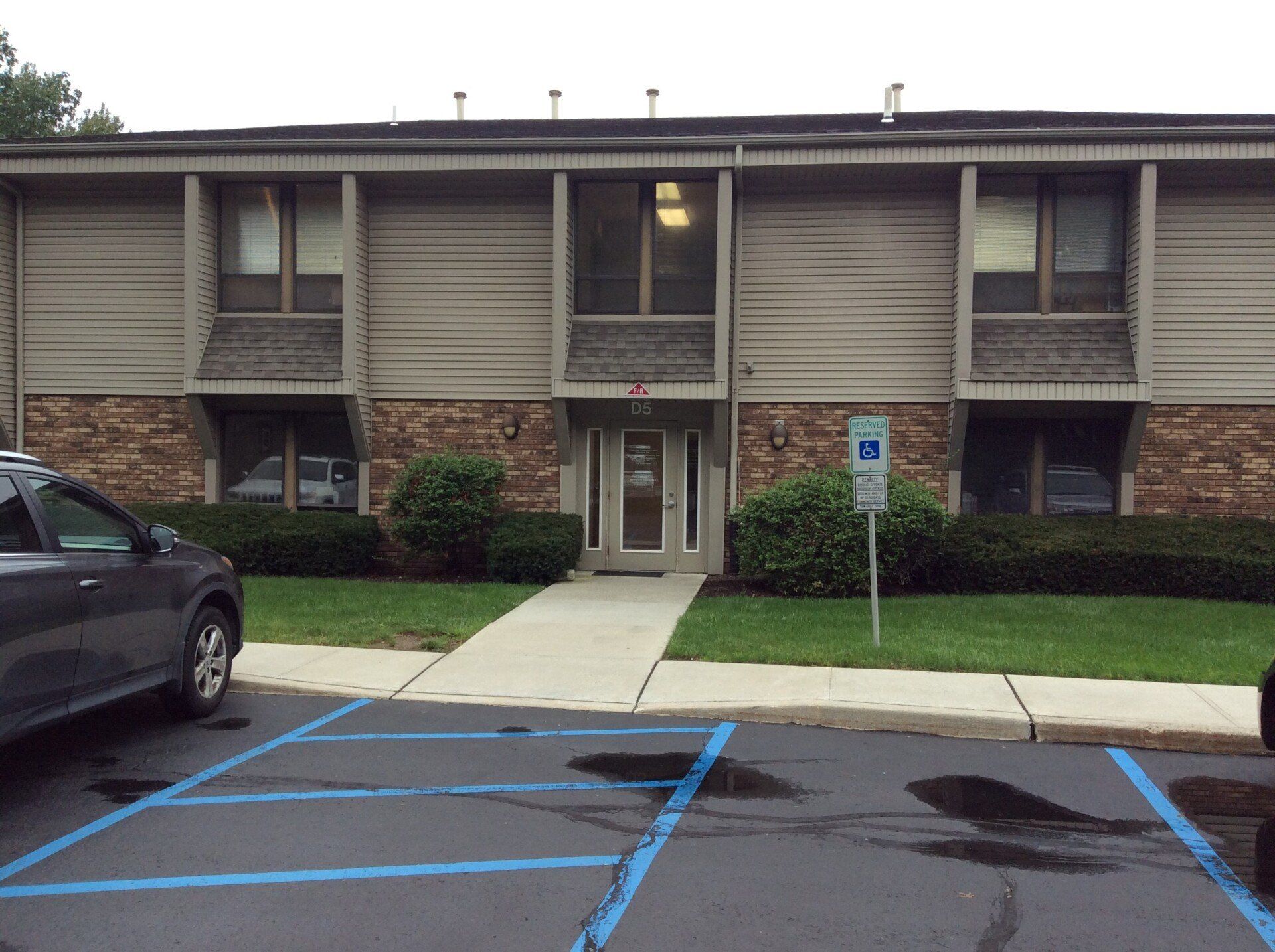 Building entrance with a walkway, handicap parking sign, and a parked car.