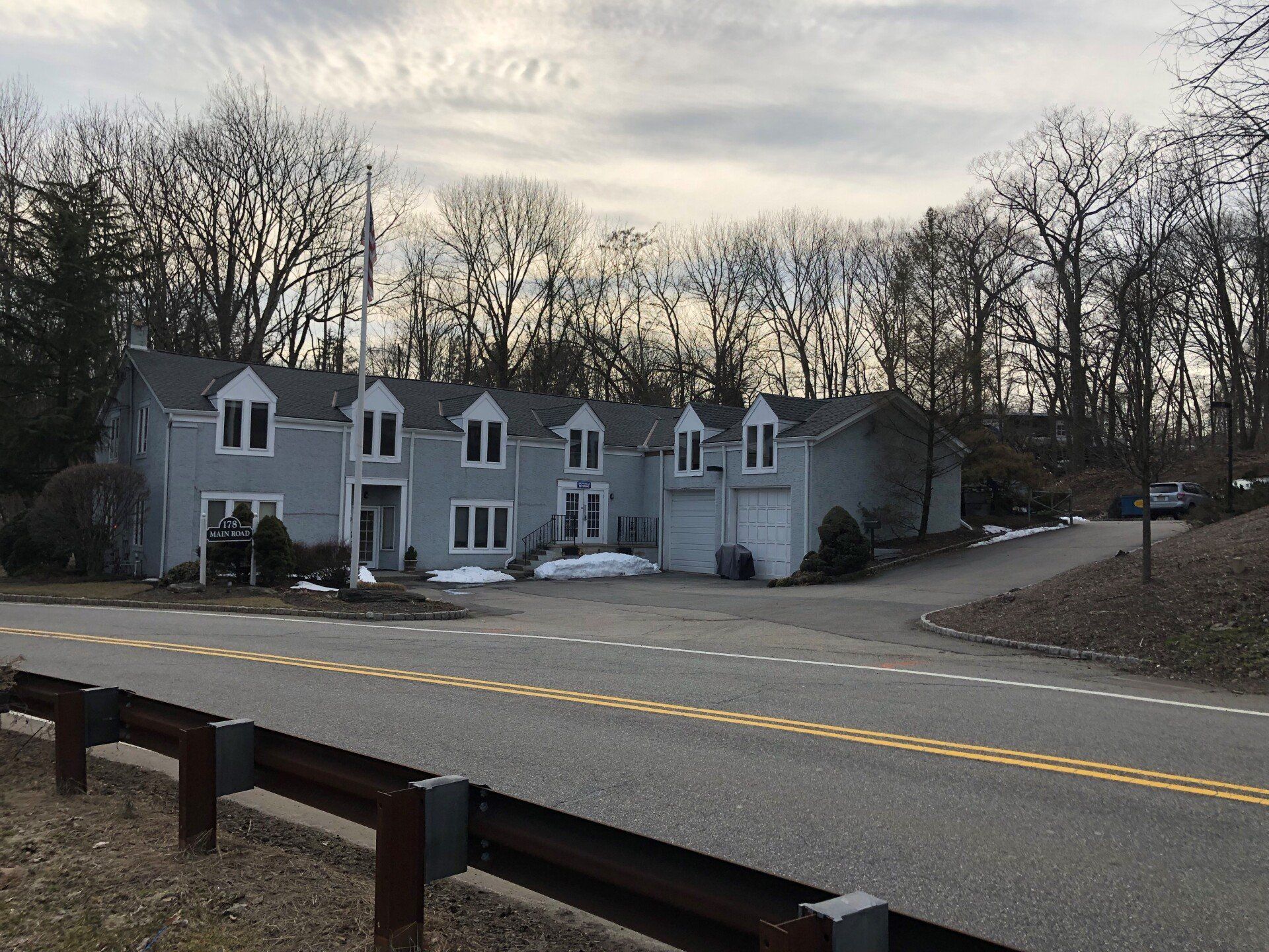 Gray house with multiple dormers and a two-car garage, accessed by a curving driveway on a cloudy day.